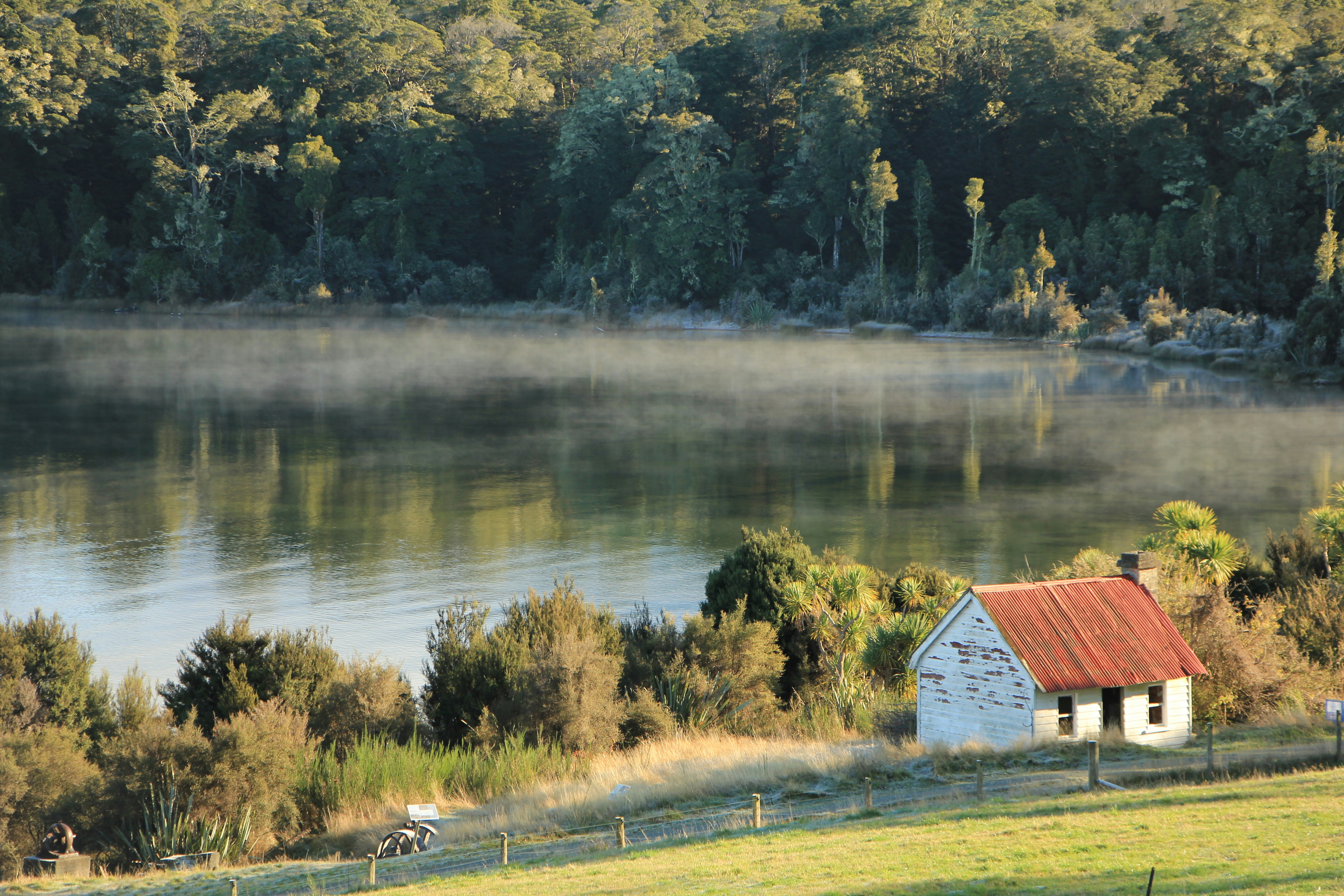 Small rustic cabin by a misty lake at sunrise.