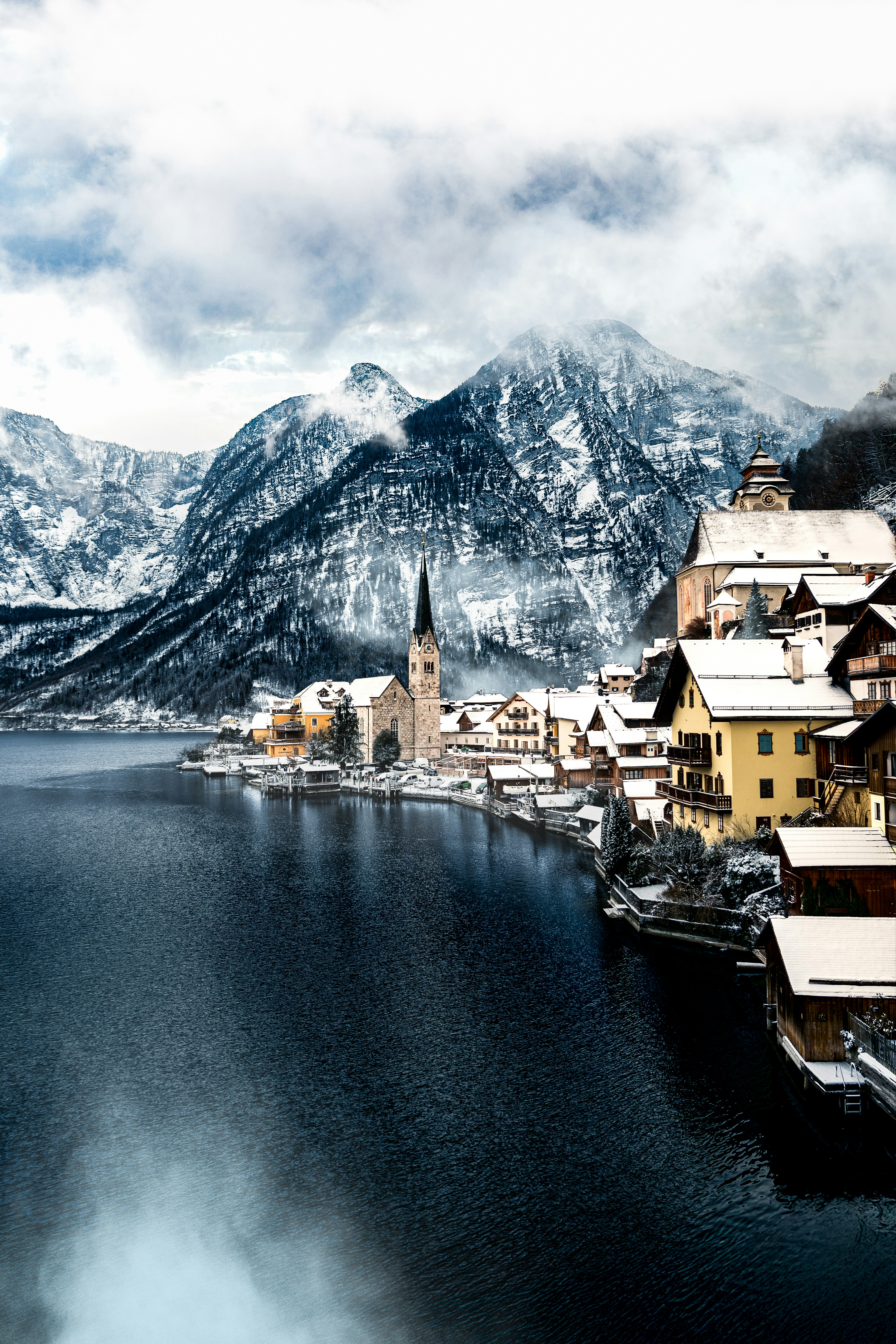 Pueblo cubierto de nieve junto a un lago oscuro y montañas.