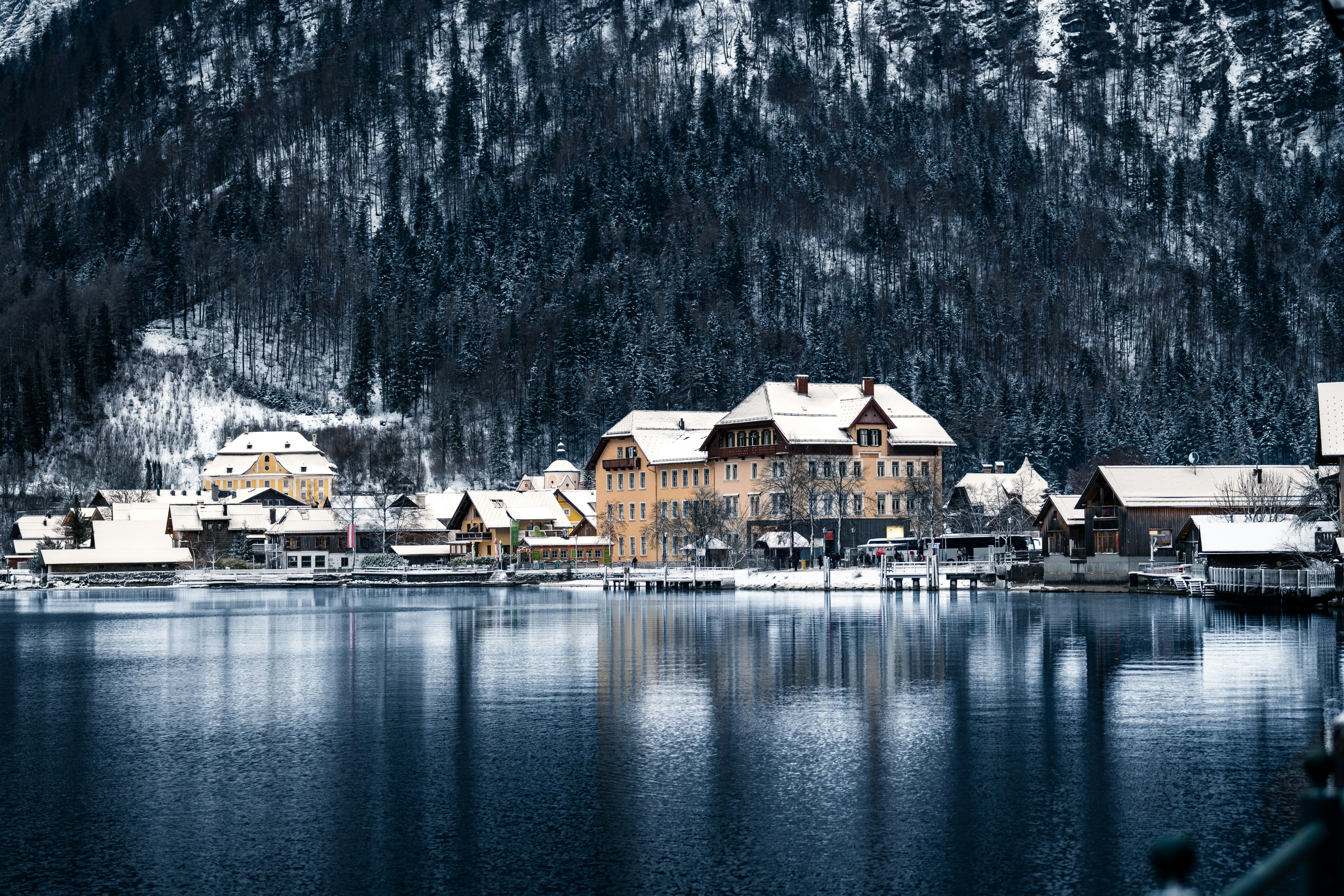Edificios cubiertos de nieve junto a un lago con montañas.