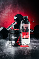 Creatine supplement, water bottle, and dumbbells on wet surface.