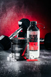 Creatine supplement, water bottle, and dumbbells on wet surface.