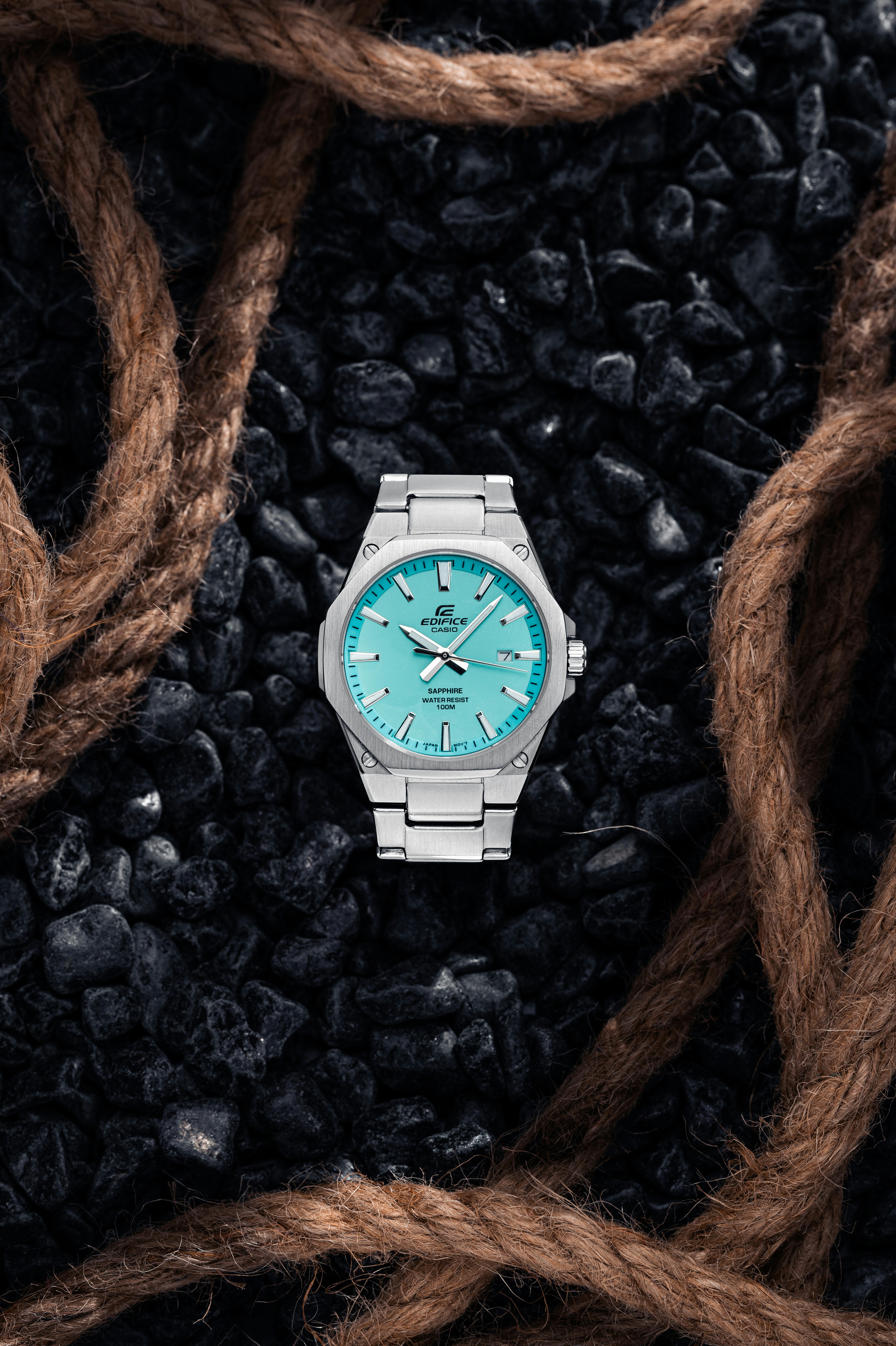 A silver watch with a turquoise dial on dark stones