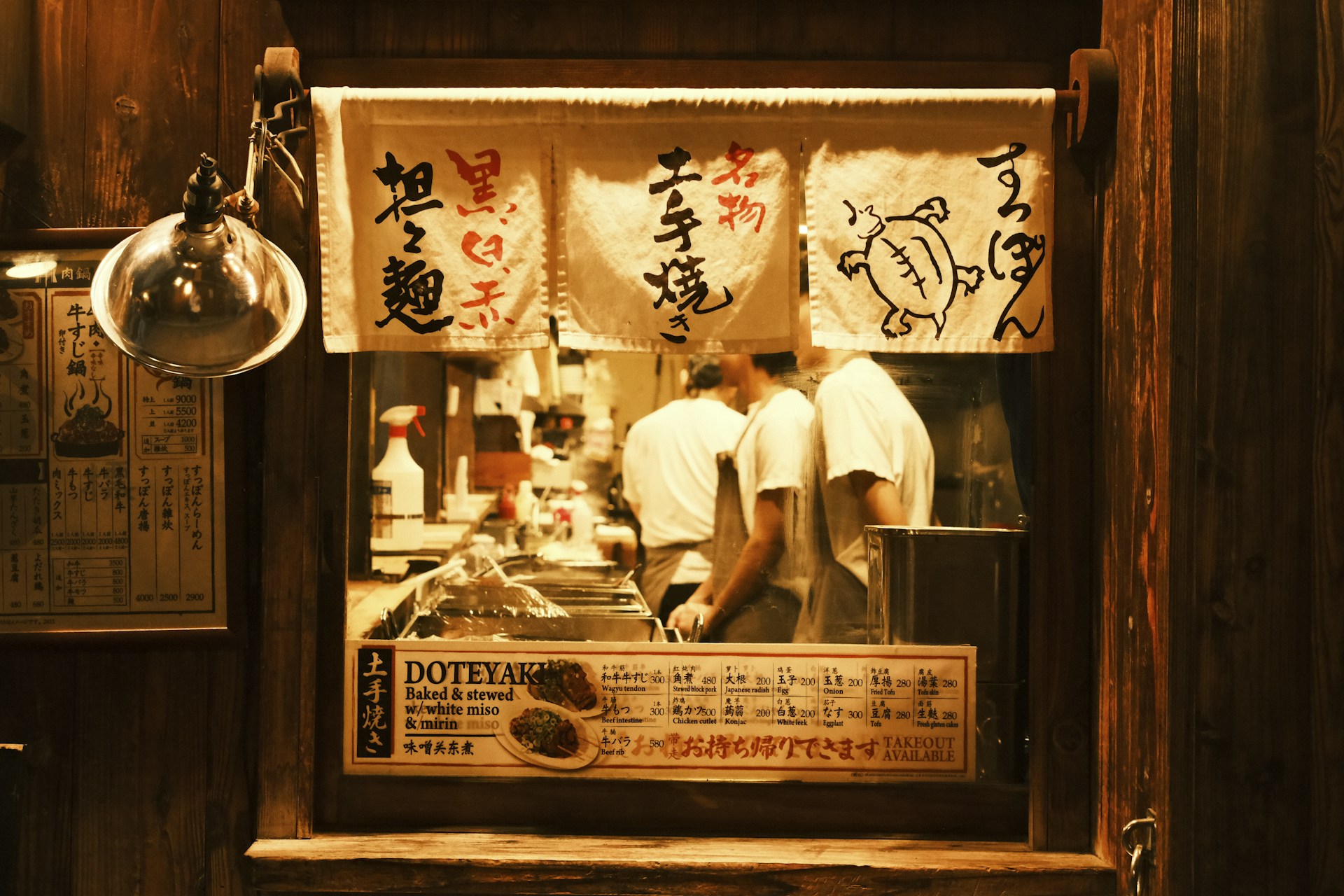 Chefs preparing food behind a japanese restaurant curtain.