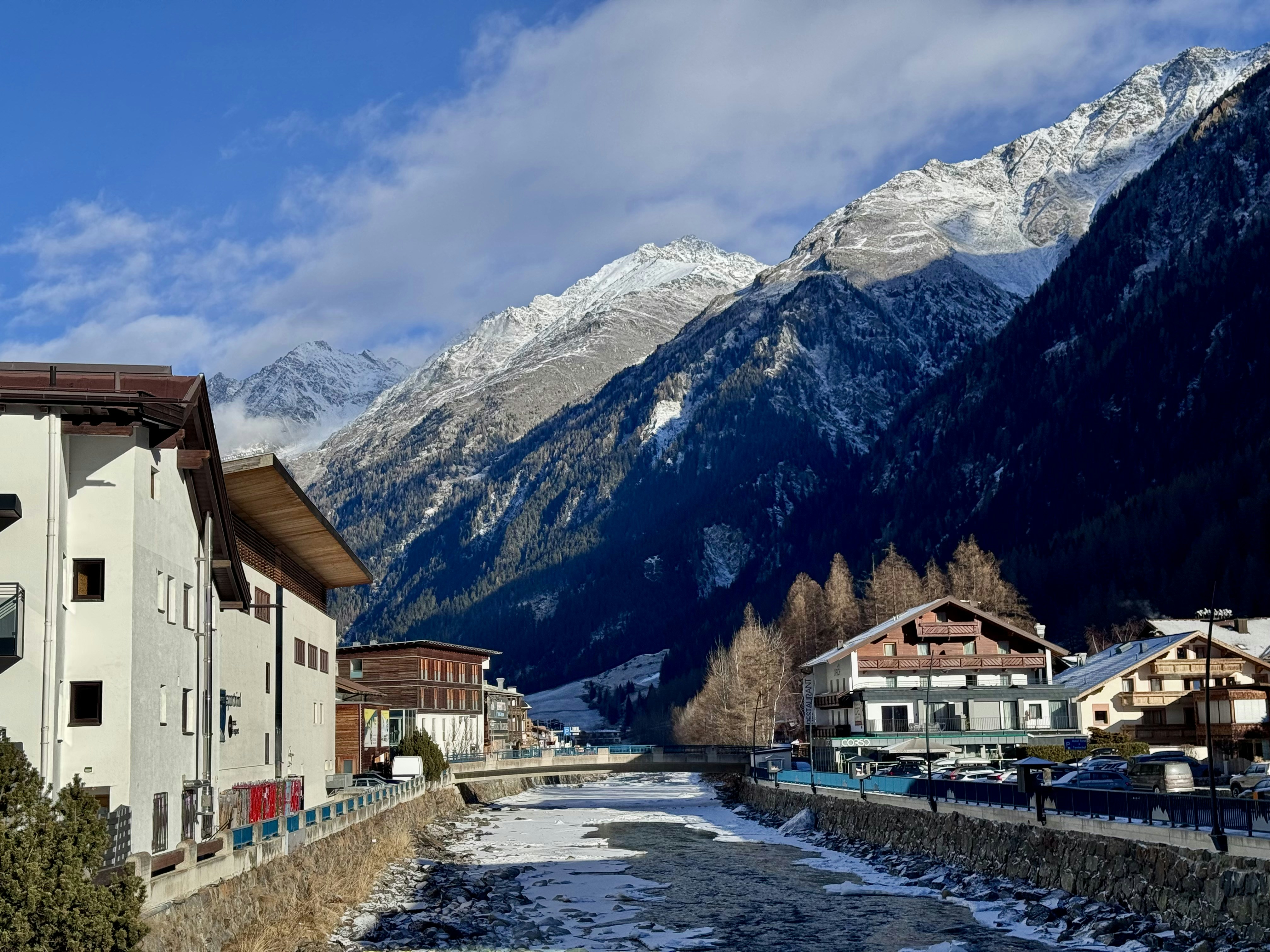 Snowy mountains overlook a village with a river.