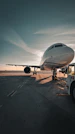 Airplane on tarmac at sunset with dramatic sky.