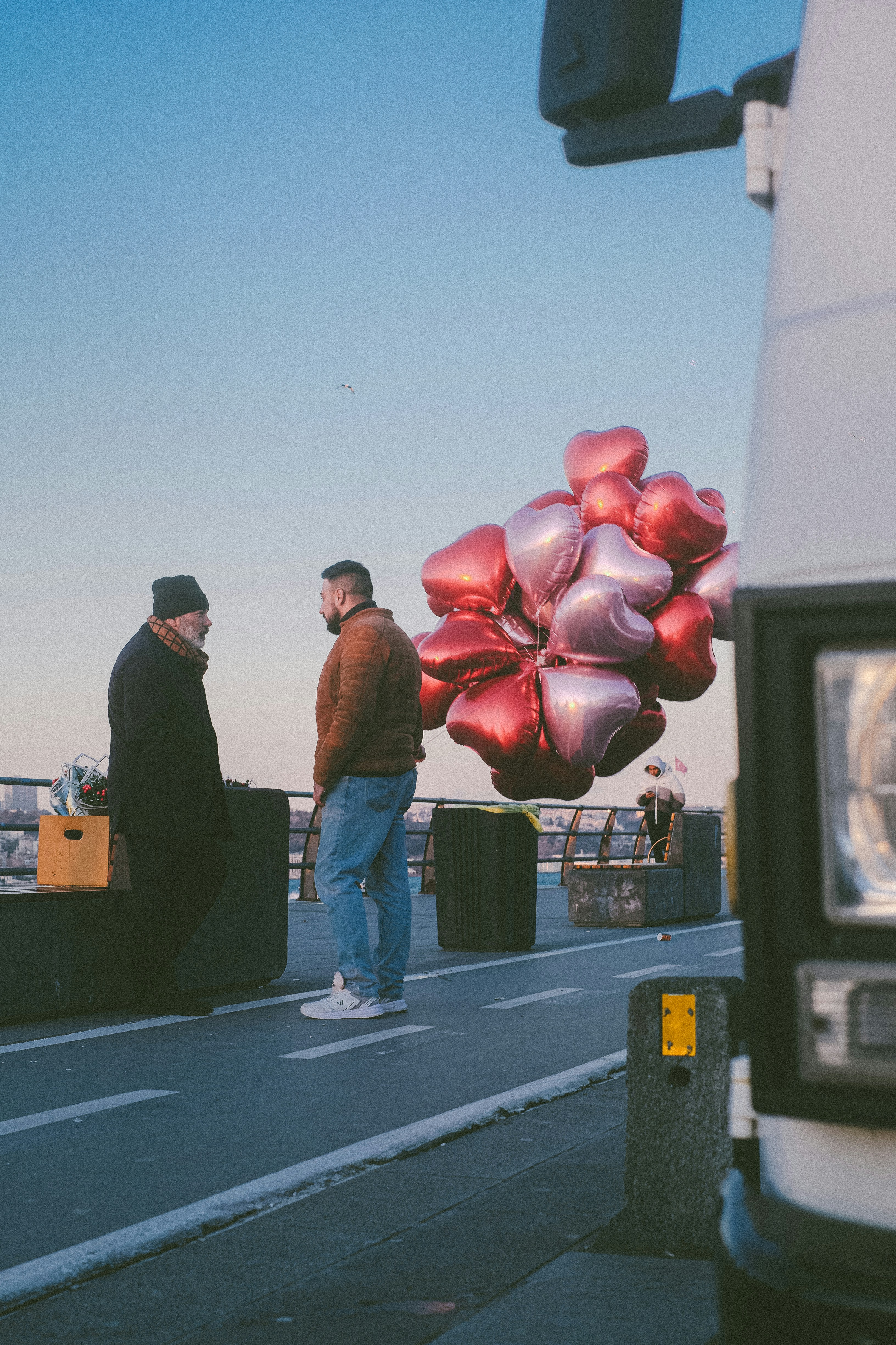 Two men and heart-shaped balloons on a walkway.