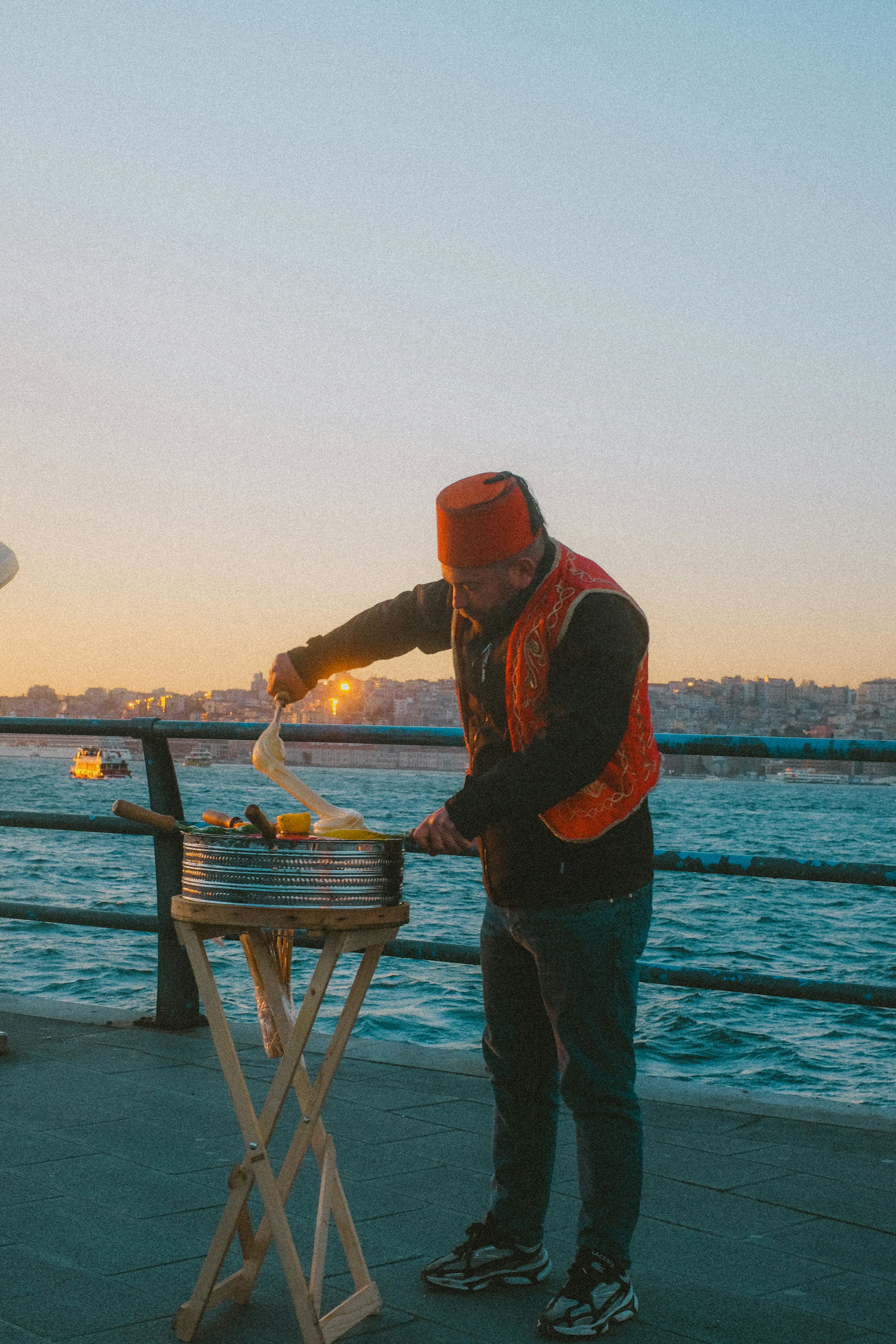 Man in fez hat prepares food by the water