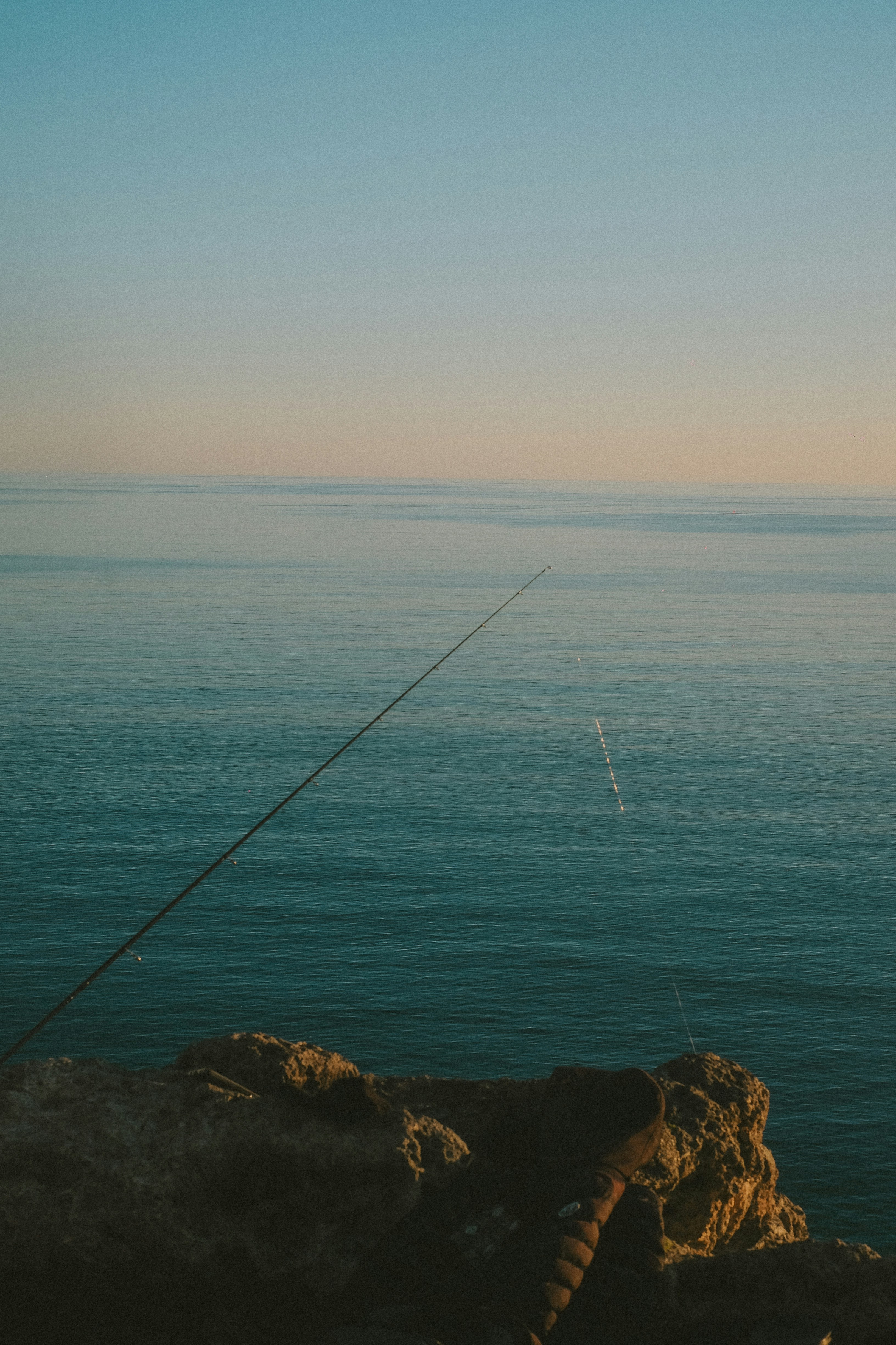 Fishing rod casting line over calm ocean waters.