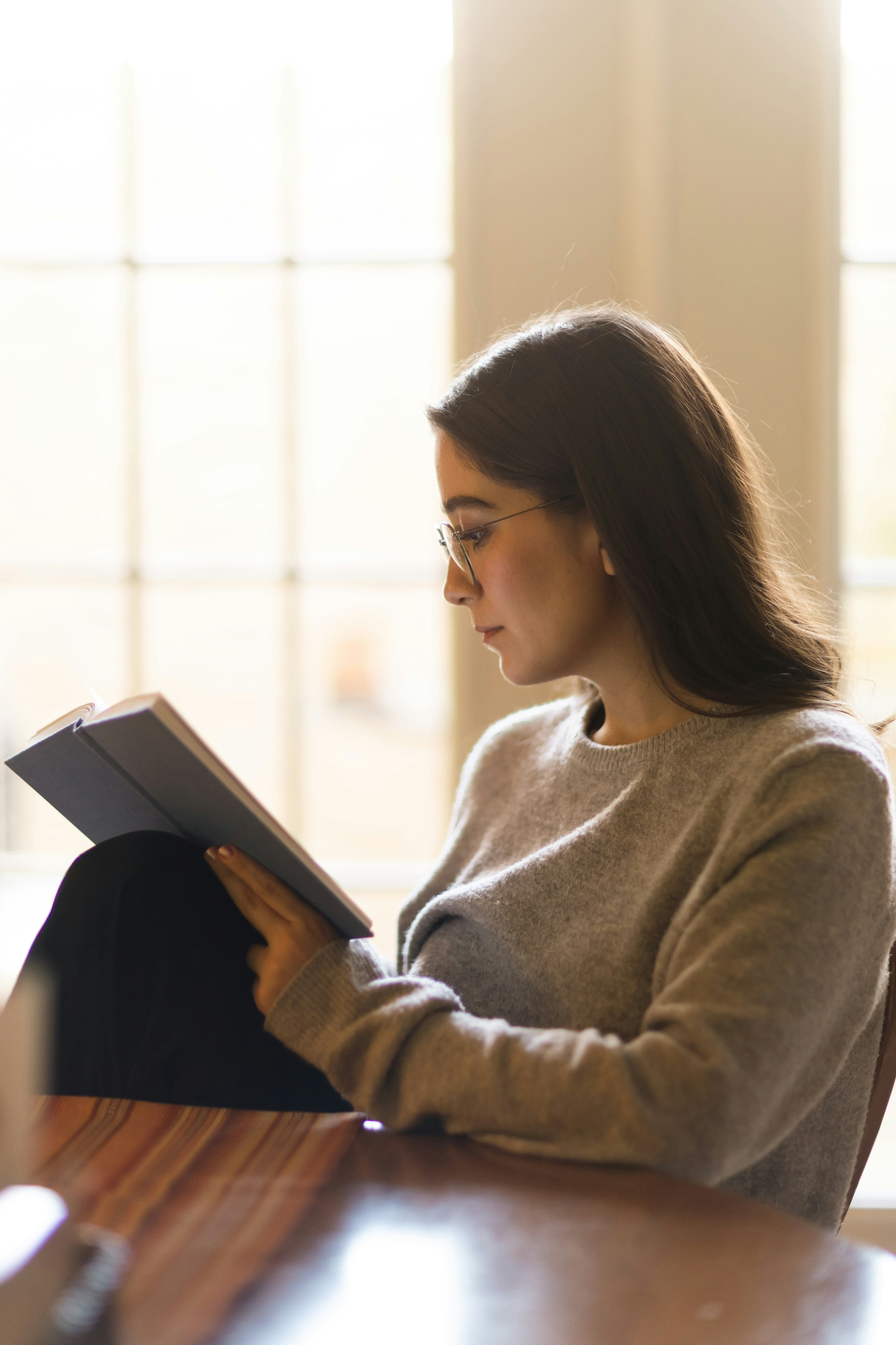 A young woman wearing glasses reads a book.