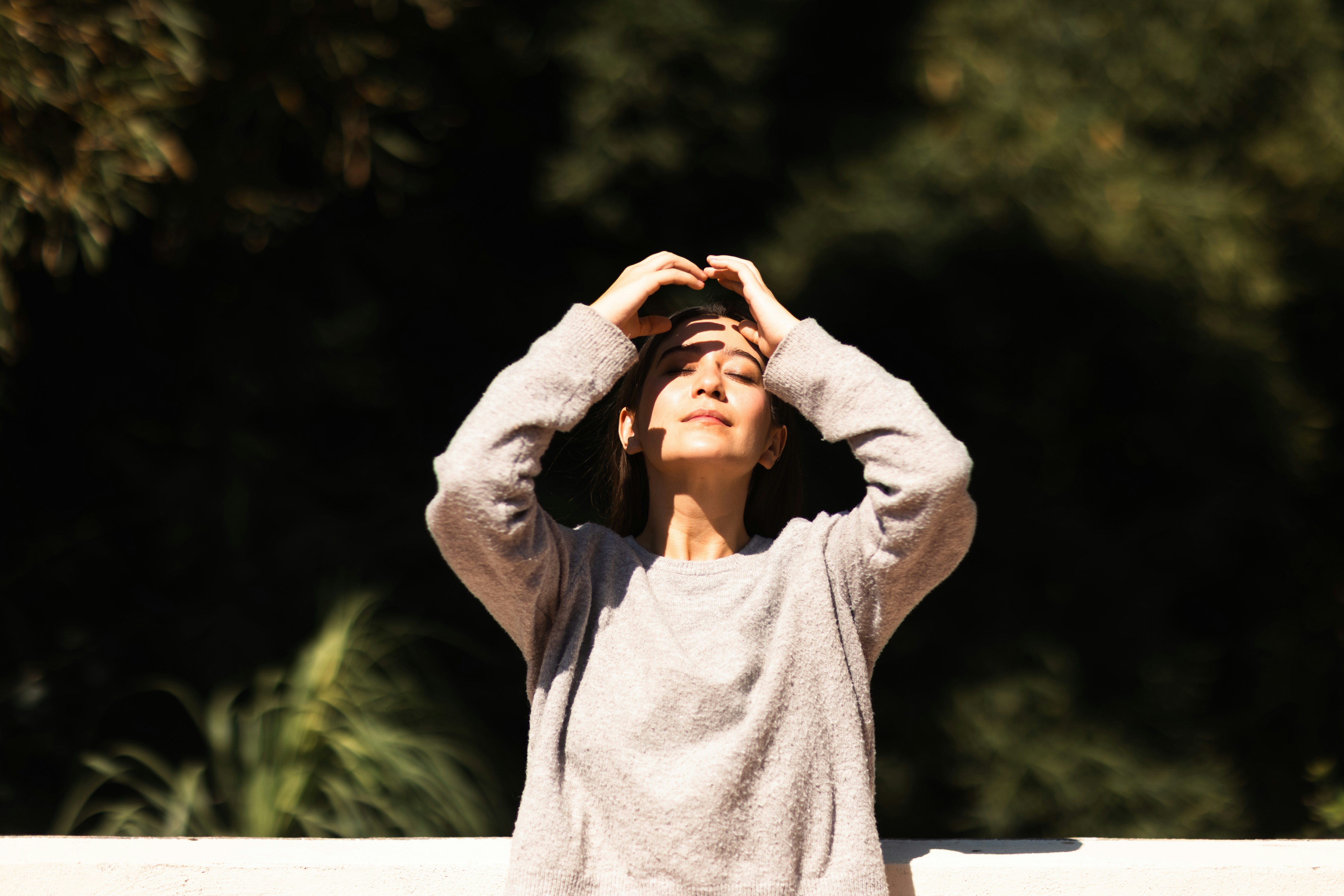 A woman with hands on her head in sunlight.