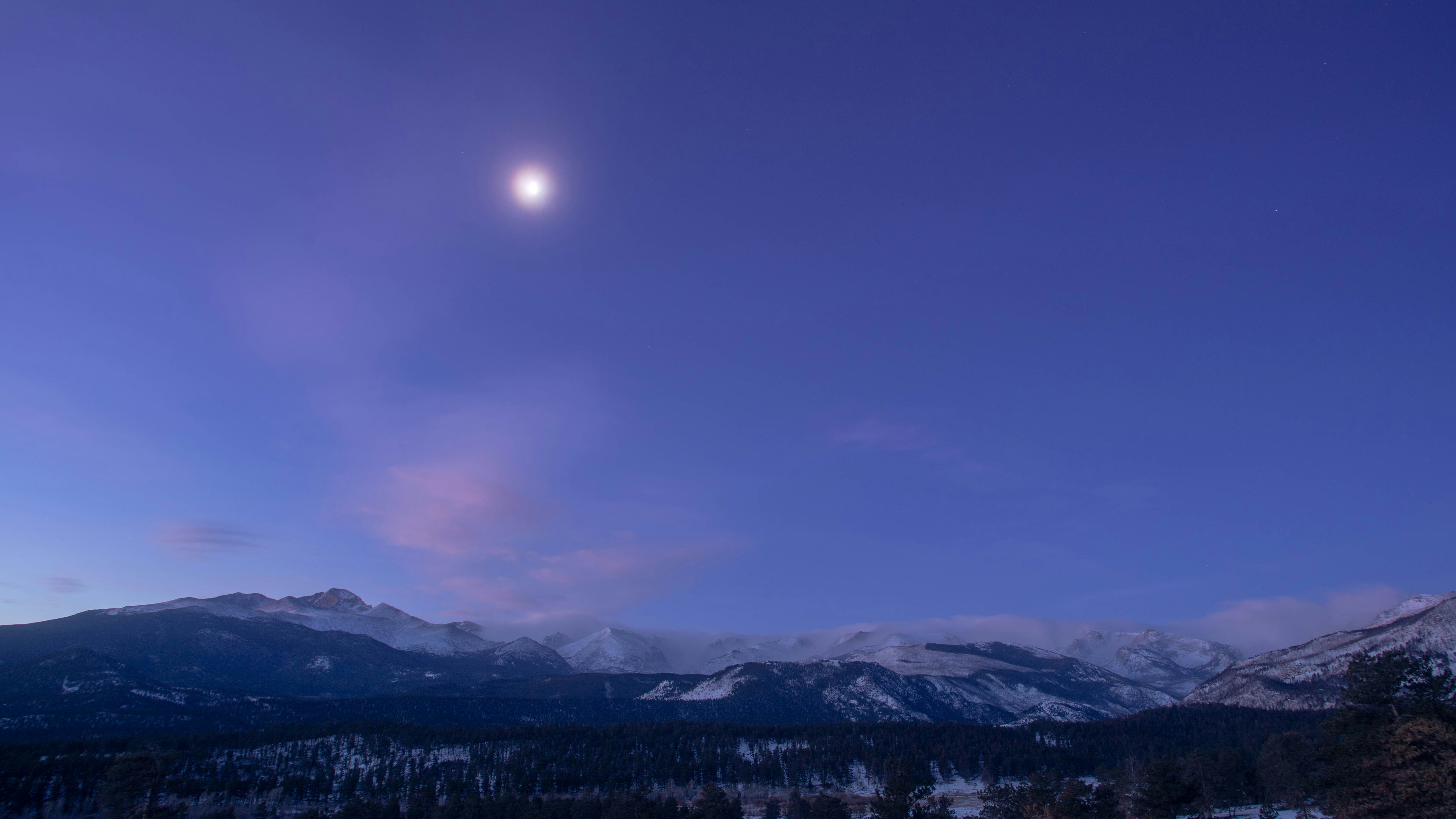 Moonlit sky over snow-capped mountains at dusk