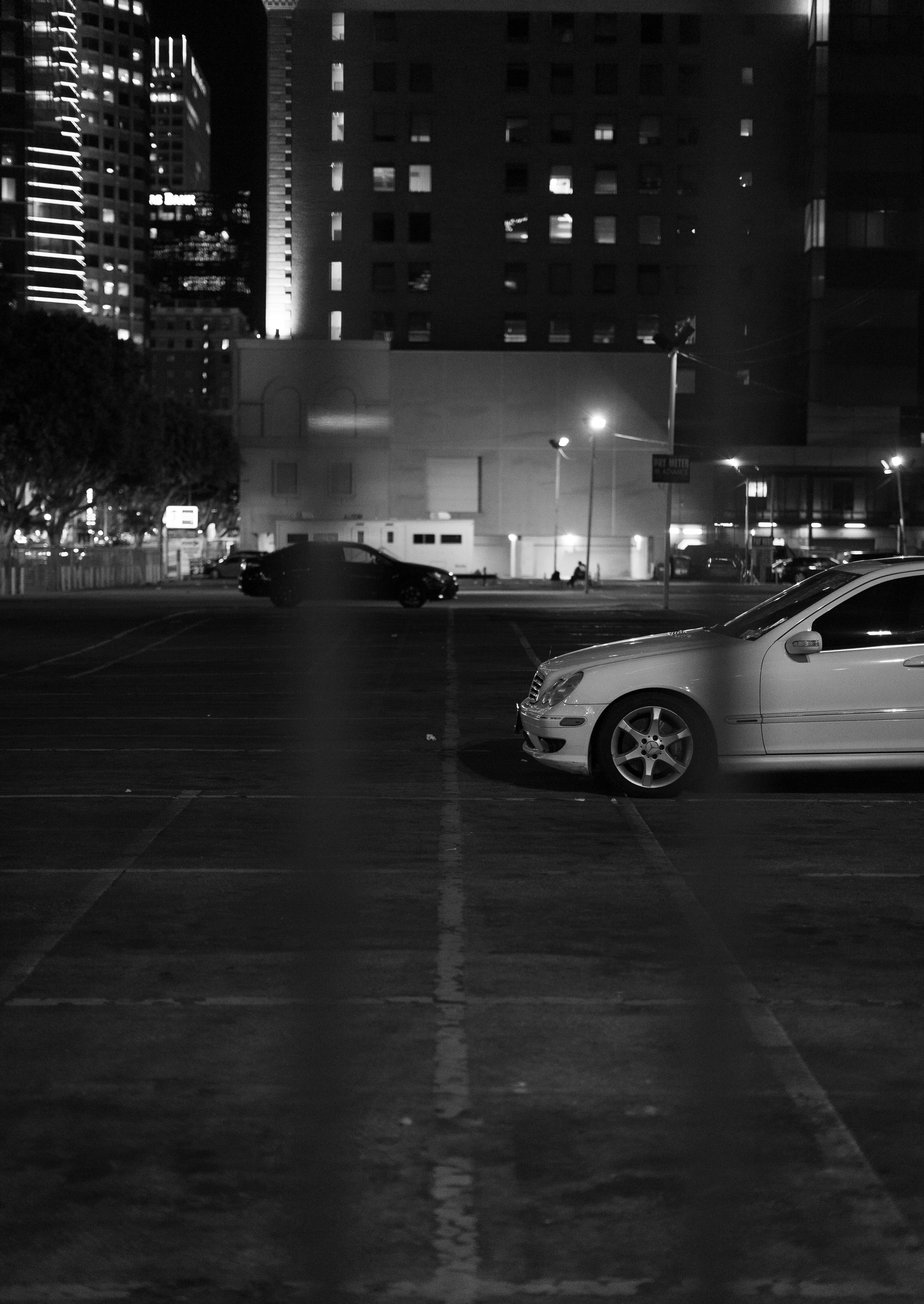 Cars parked in a lot at night with city buildings.