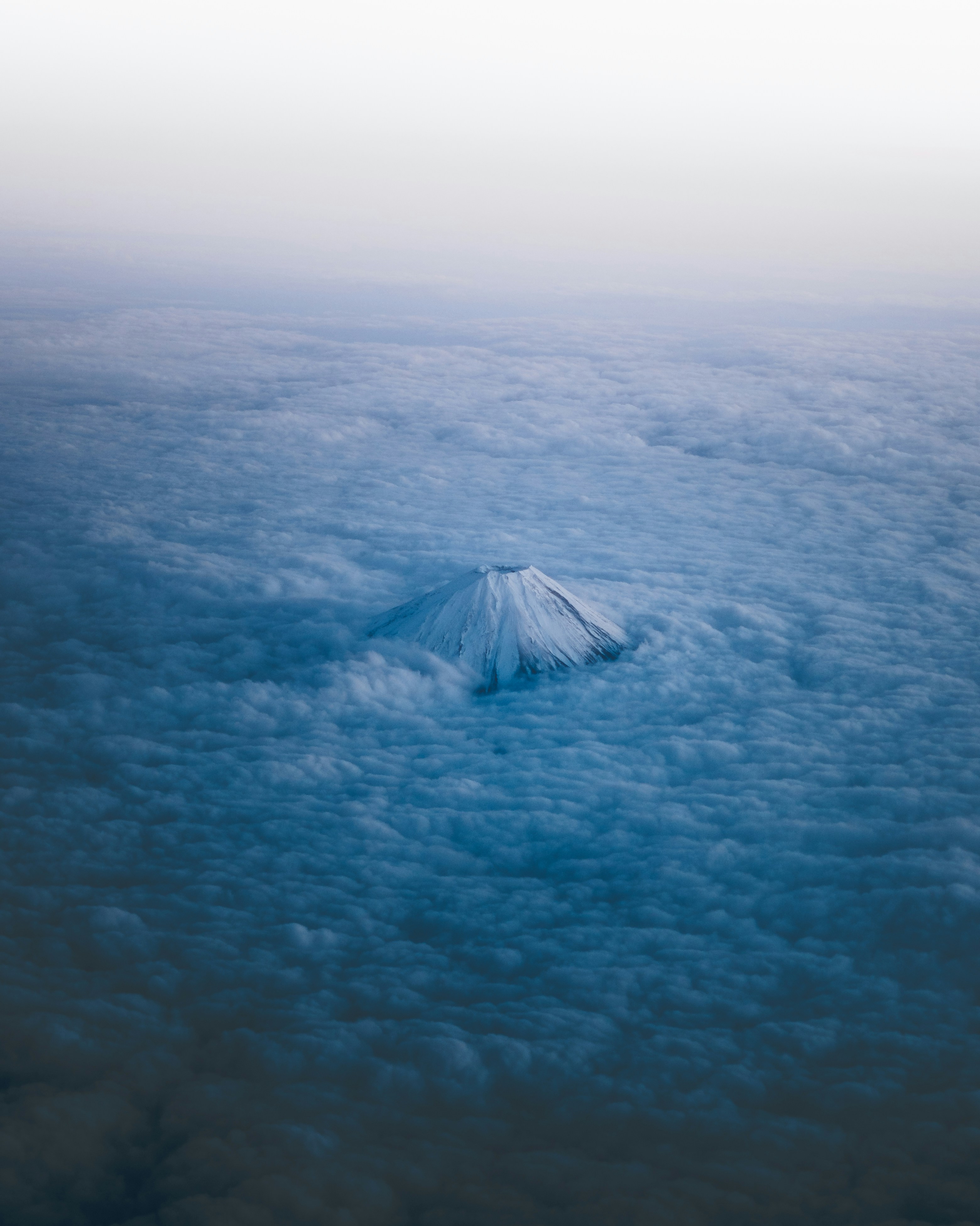 Snow-capped mountain peak emerges from clouds below