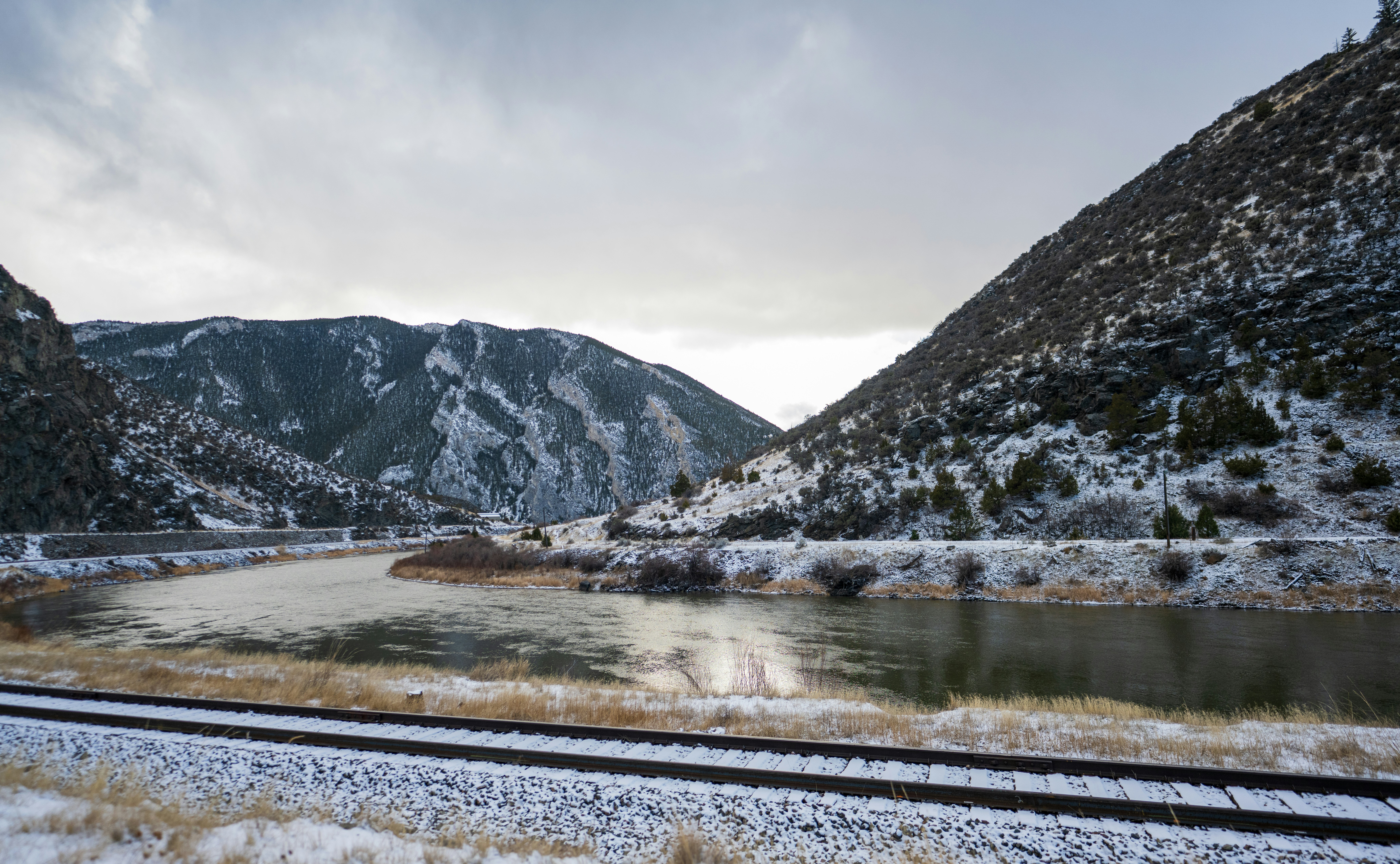 Snowy mountain valley with a river and train tracks