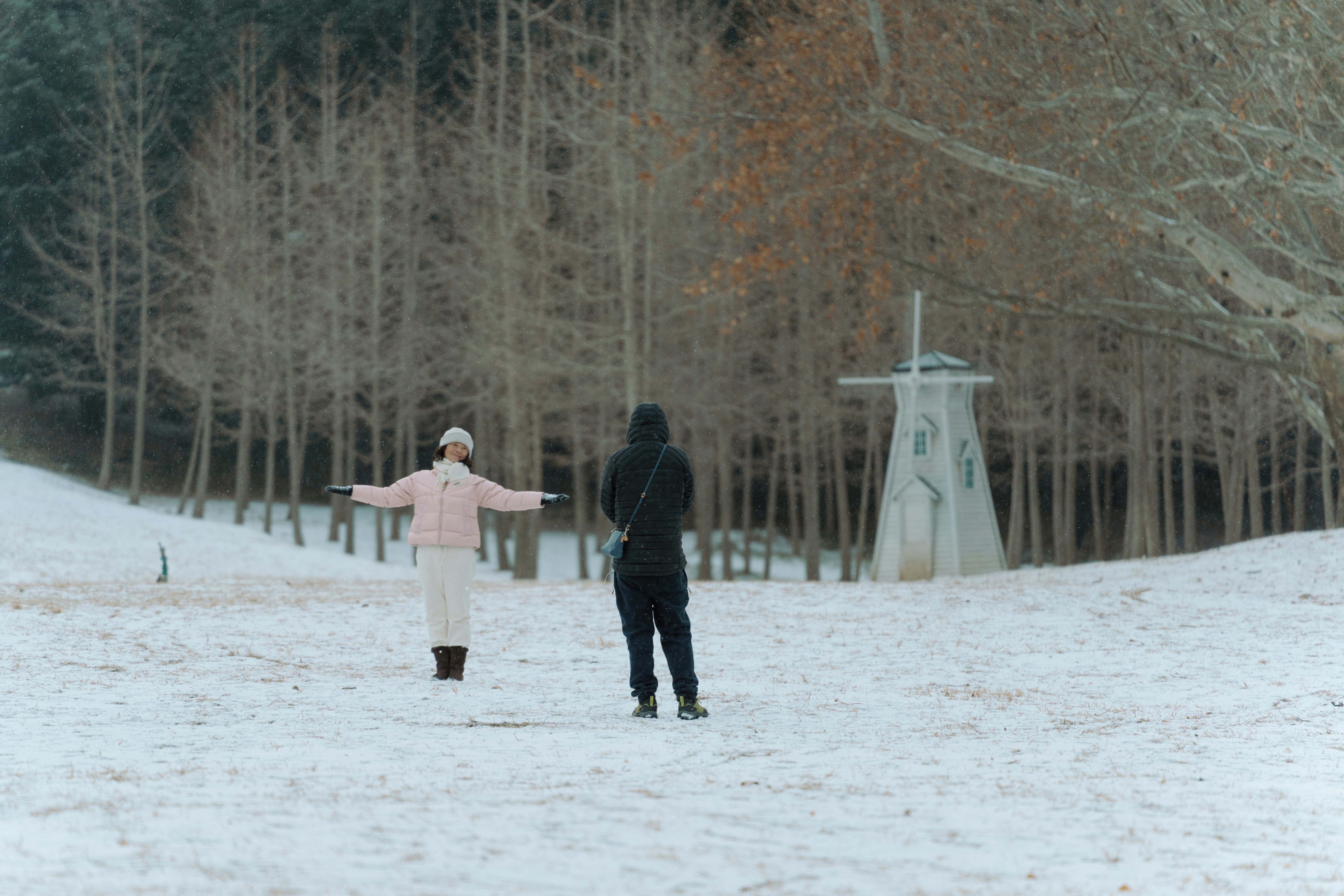 Two people in a snowy field near a windmill.