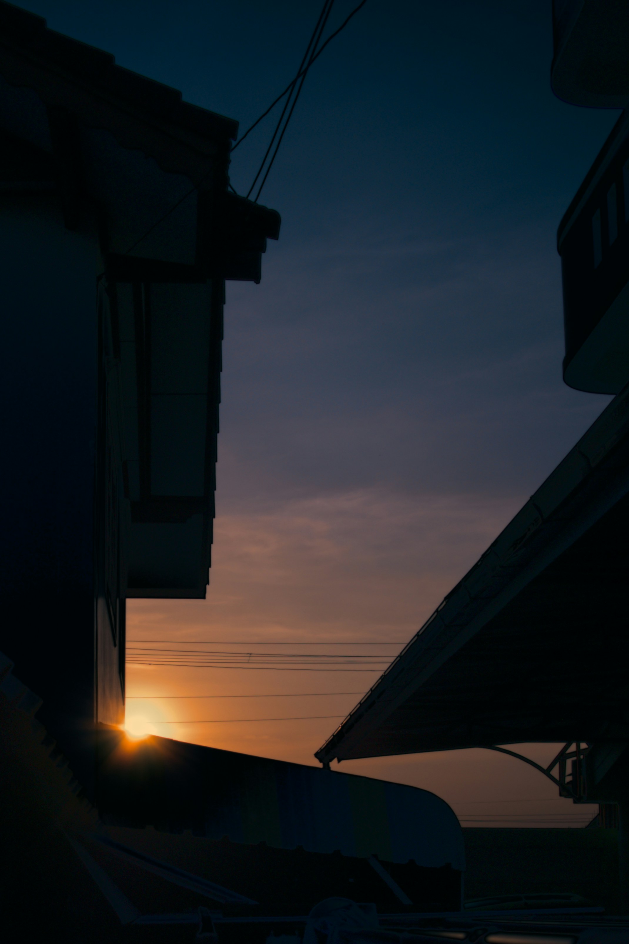 Sunset light slipping between urban rooftops, casting silhouettes and soft shadows as the day fades into night.
