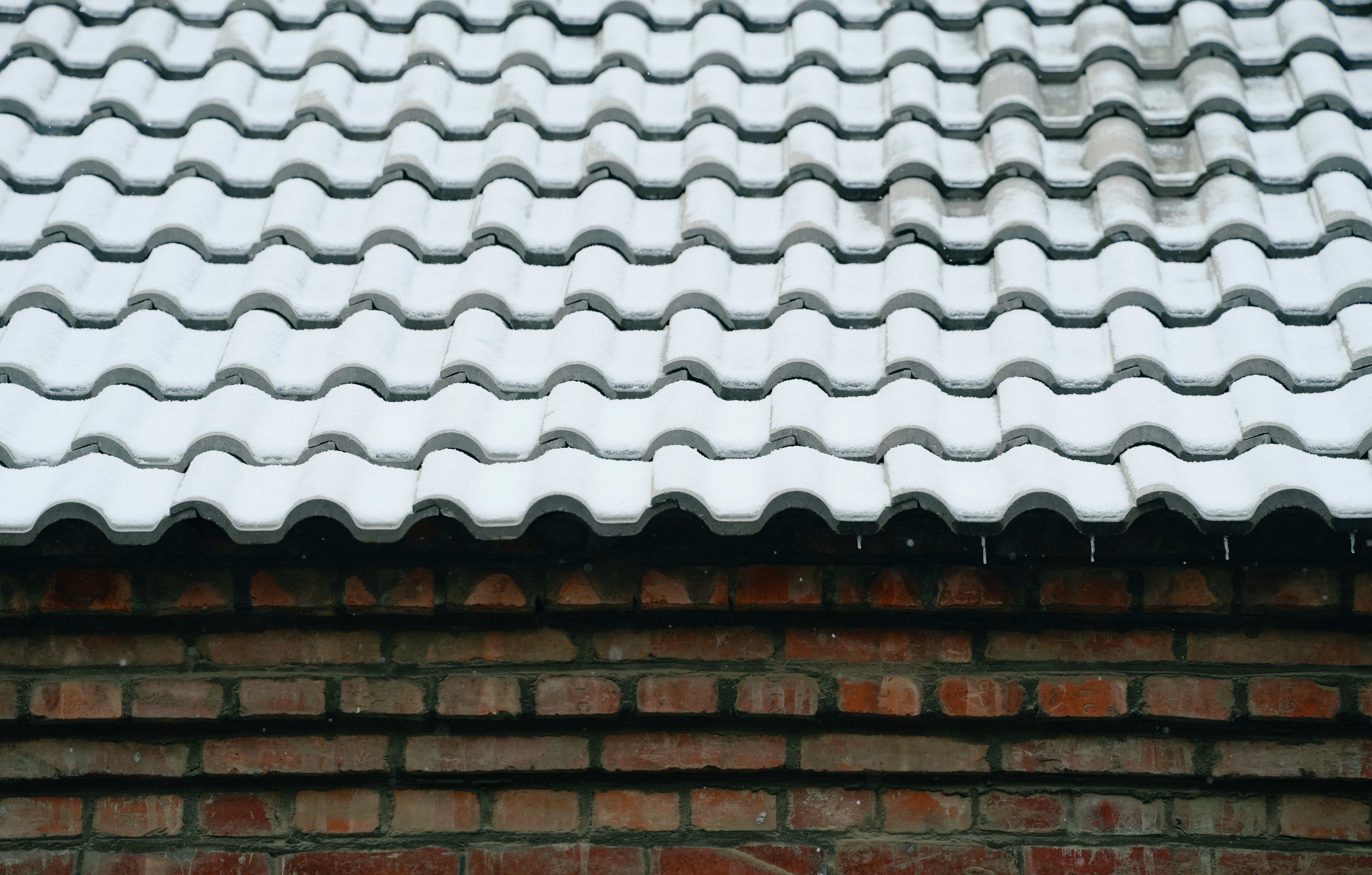 Snow-covered roof tiles above a brick wall