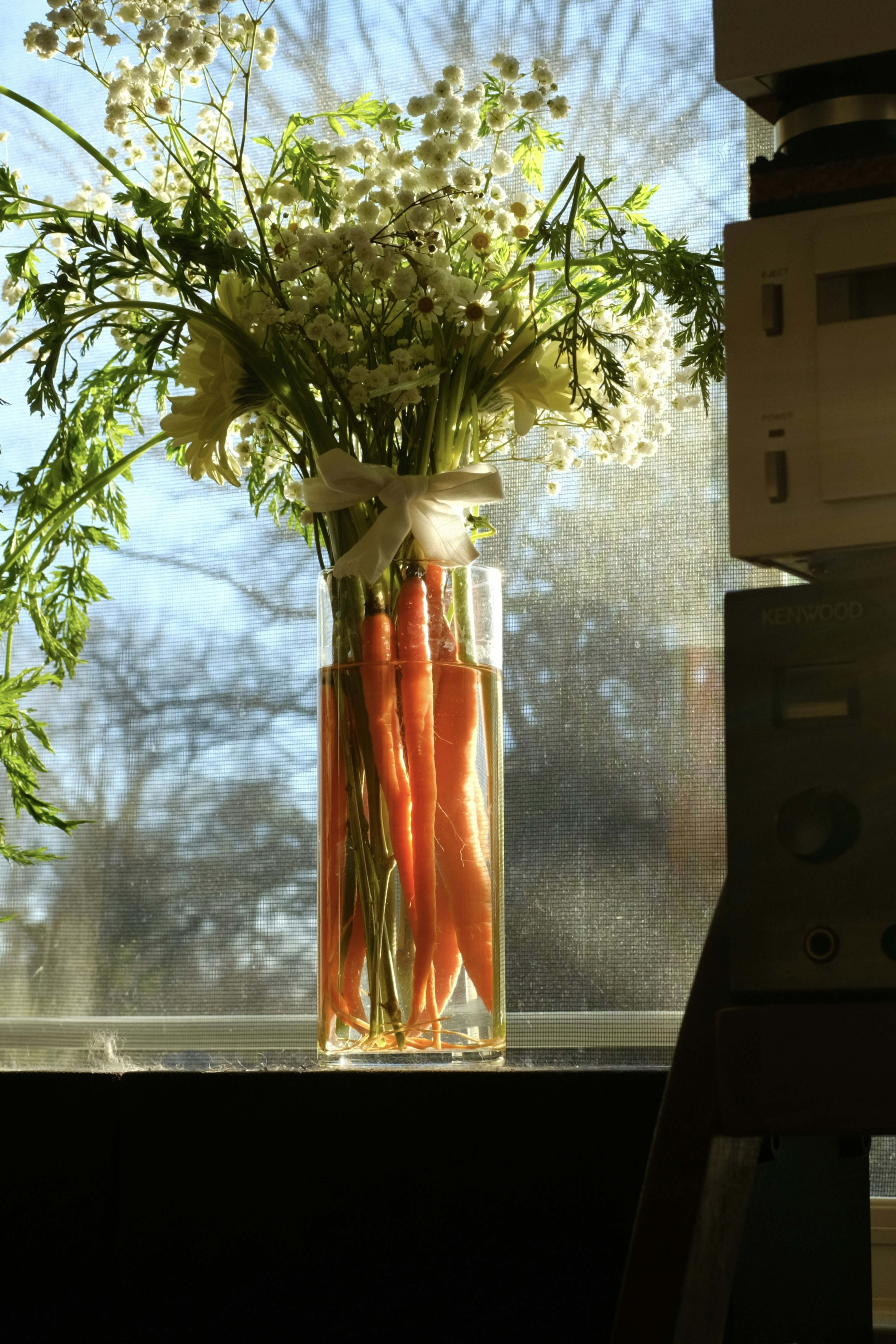 Carrots and flowers in a vase on windowsill