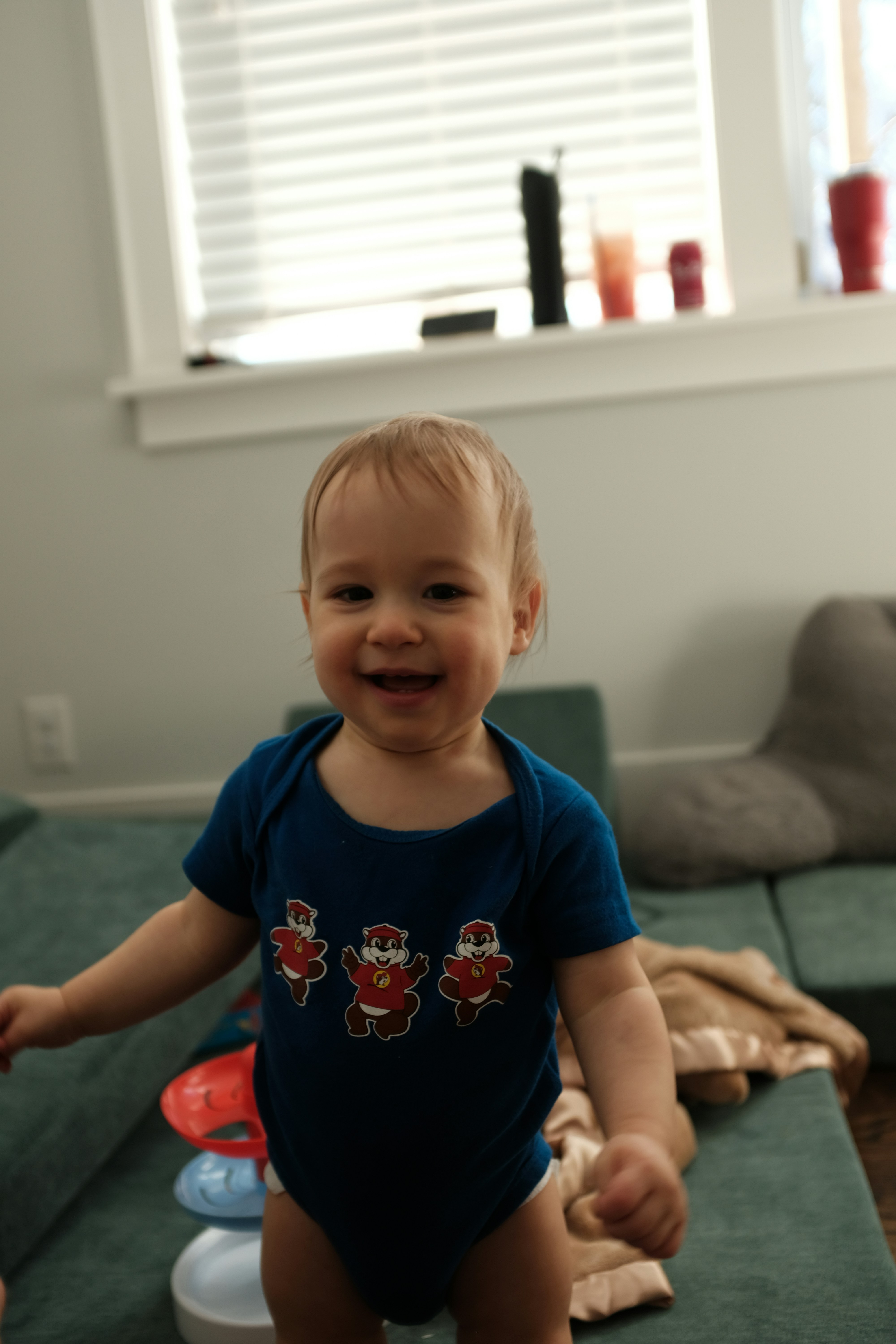 A smiling baby in a blue onesie with santa prints.