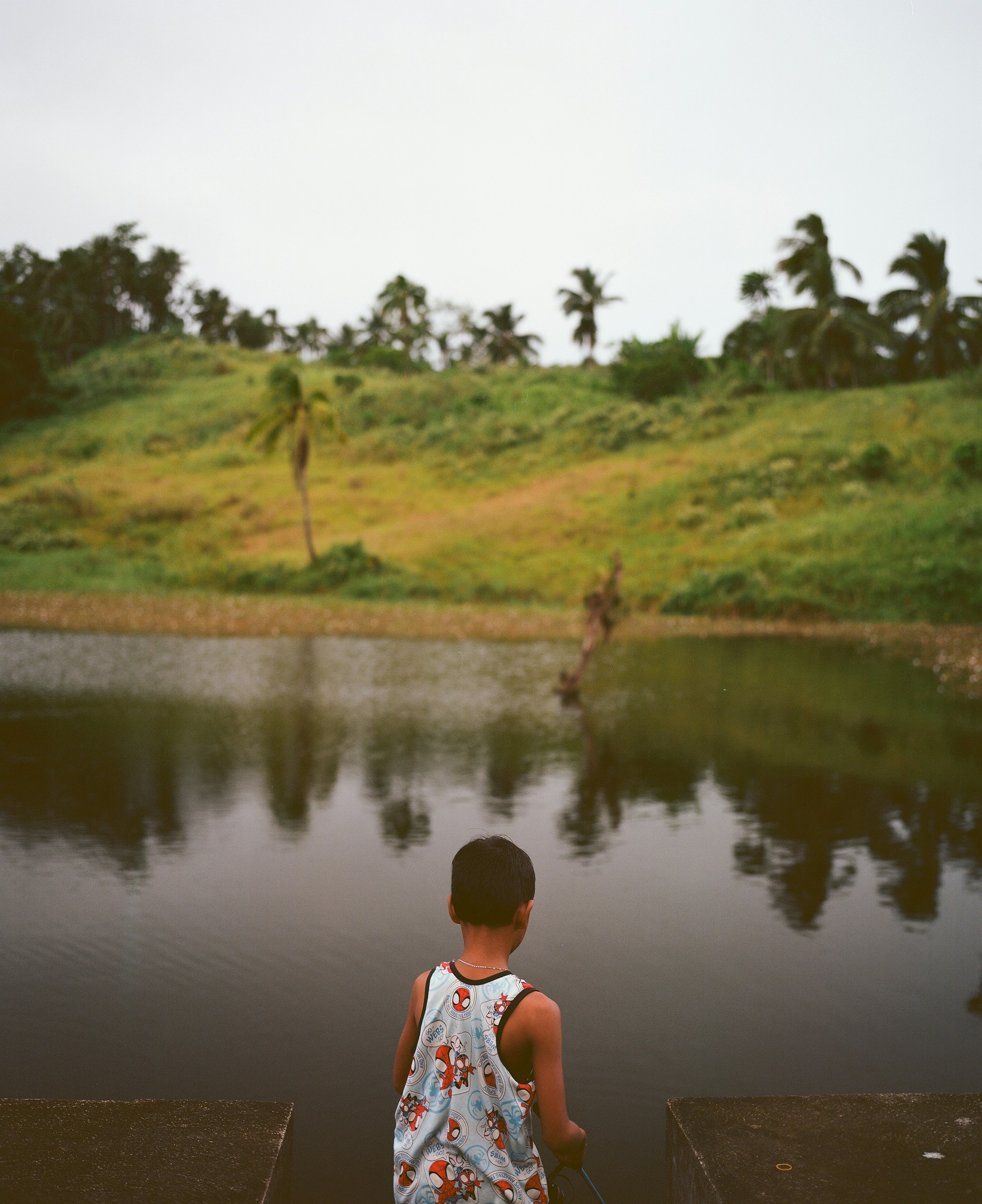 Boy looking at a calm lake with green hills