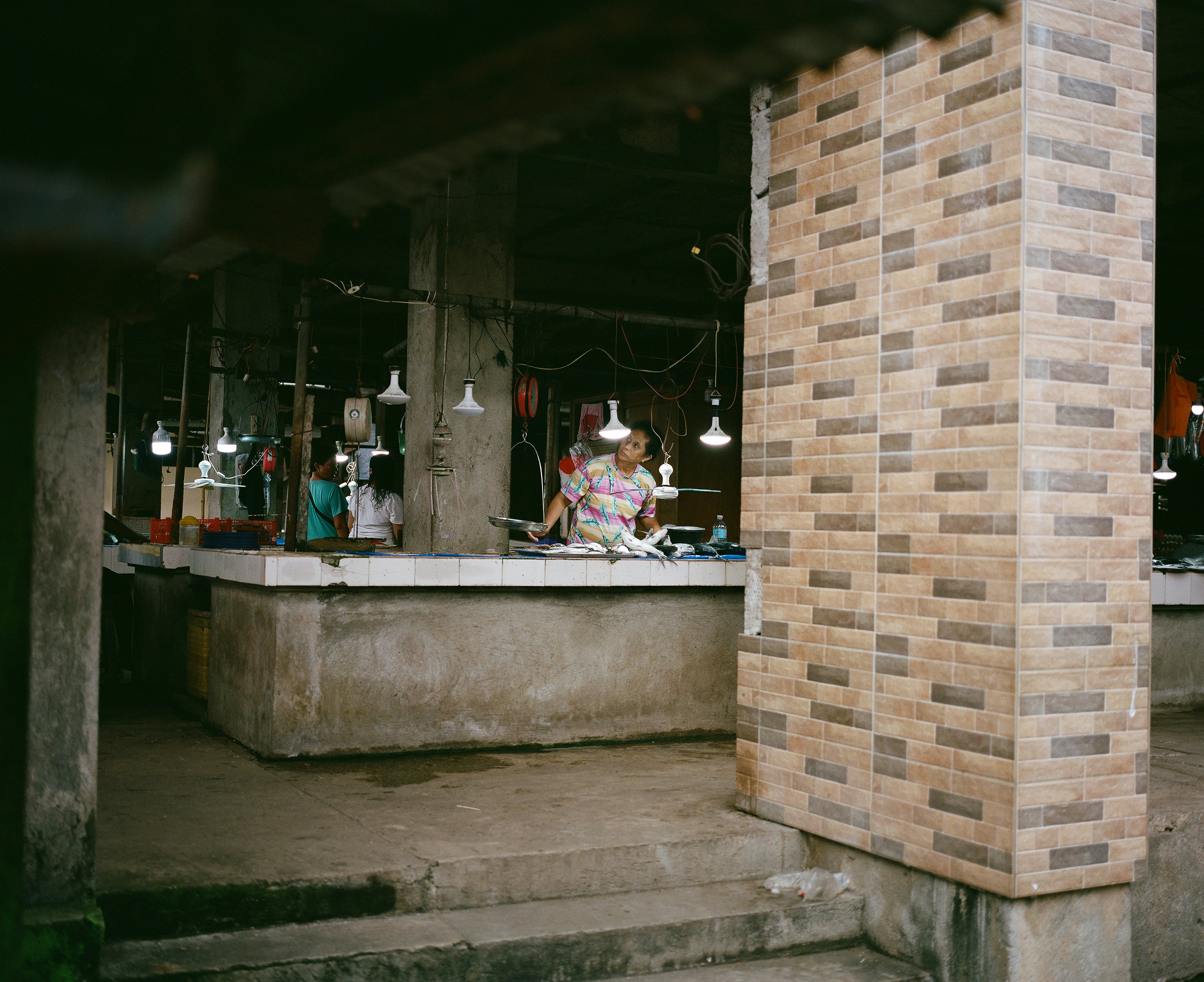 A vendor stands behind a market stall with goods displayed.