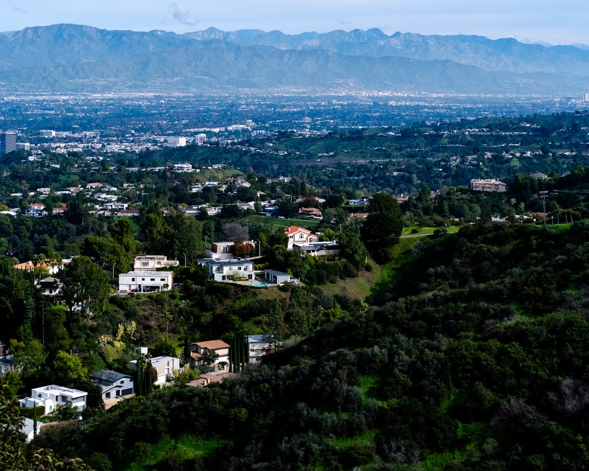 Suburban homes nestled in rolling green hills with mountains beyond representing the American housing market