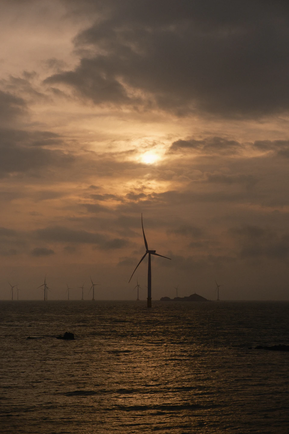 Serene sunset over ocean with large wind turbine standing tall on water's surface