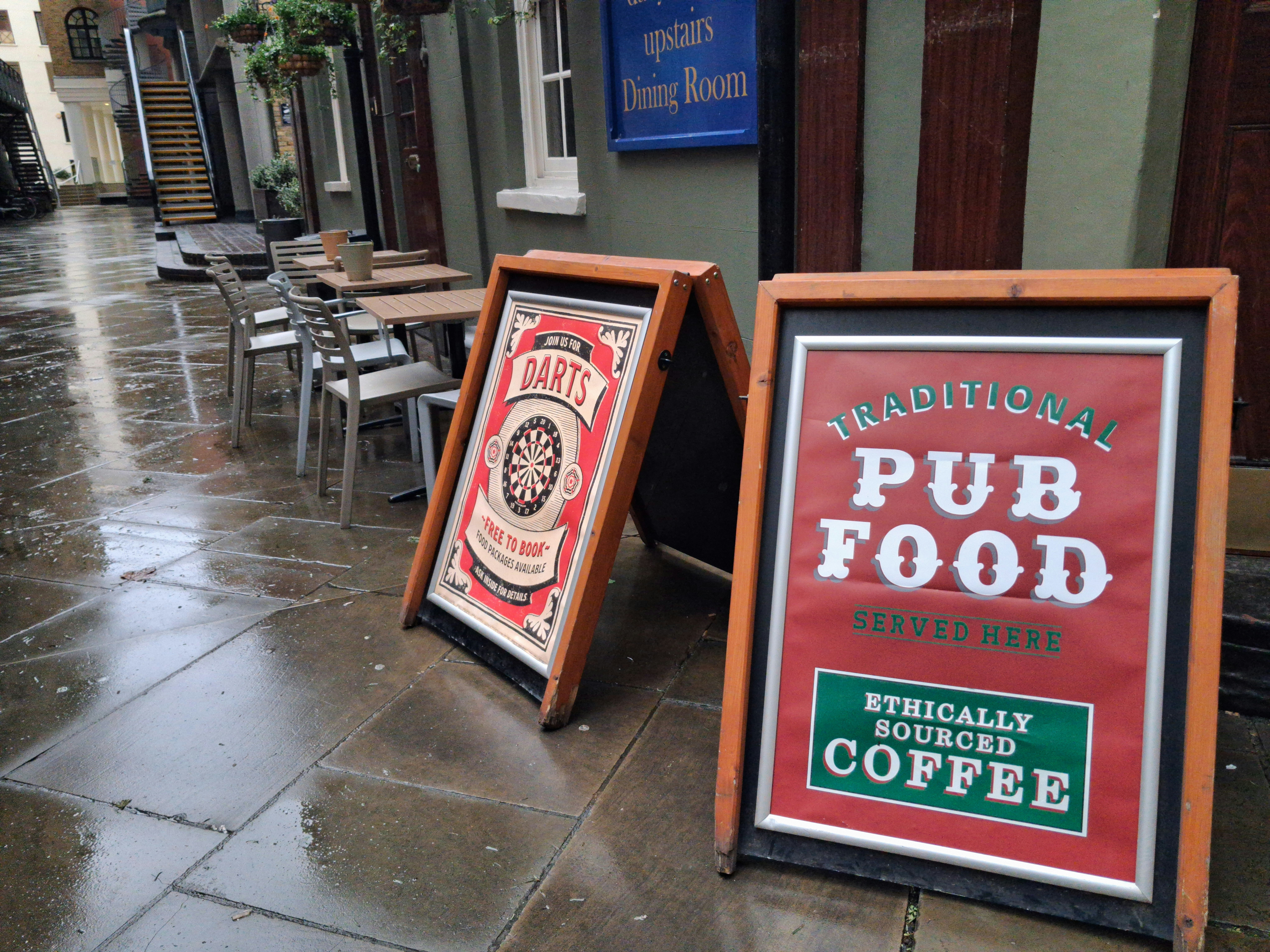 Due cartelli a A fuori da un pub su una strada bagnata.