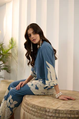 Woman in blue patterned outfit sits on wooden surface