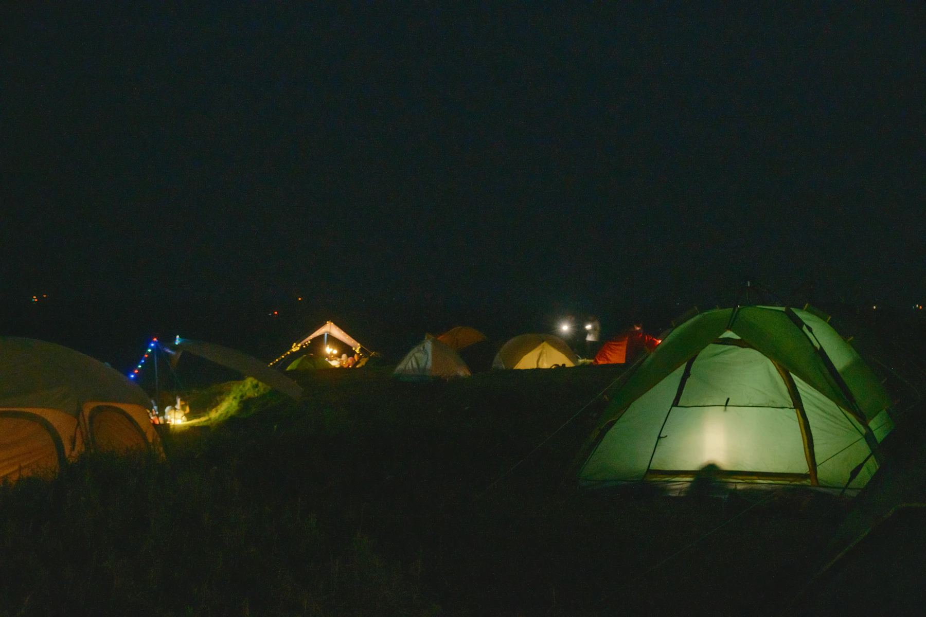 Several illuminated camping tents at an outdoor campsite at night