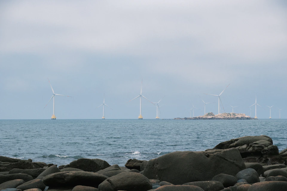 Six wind turbines stand tall on the water, contrasting white structures against blue sky