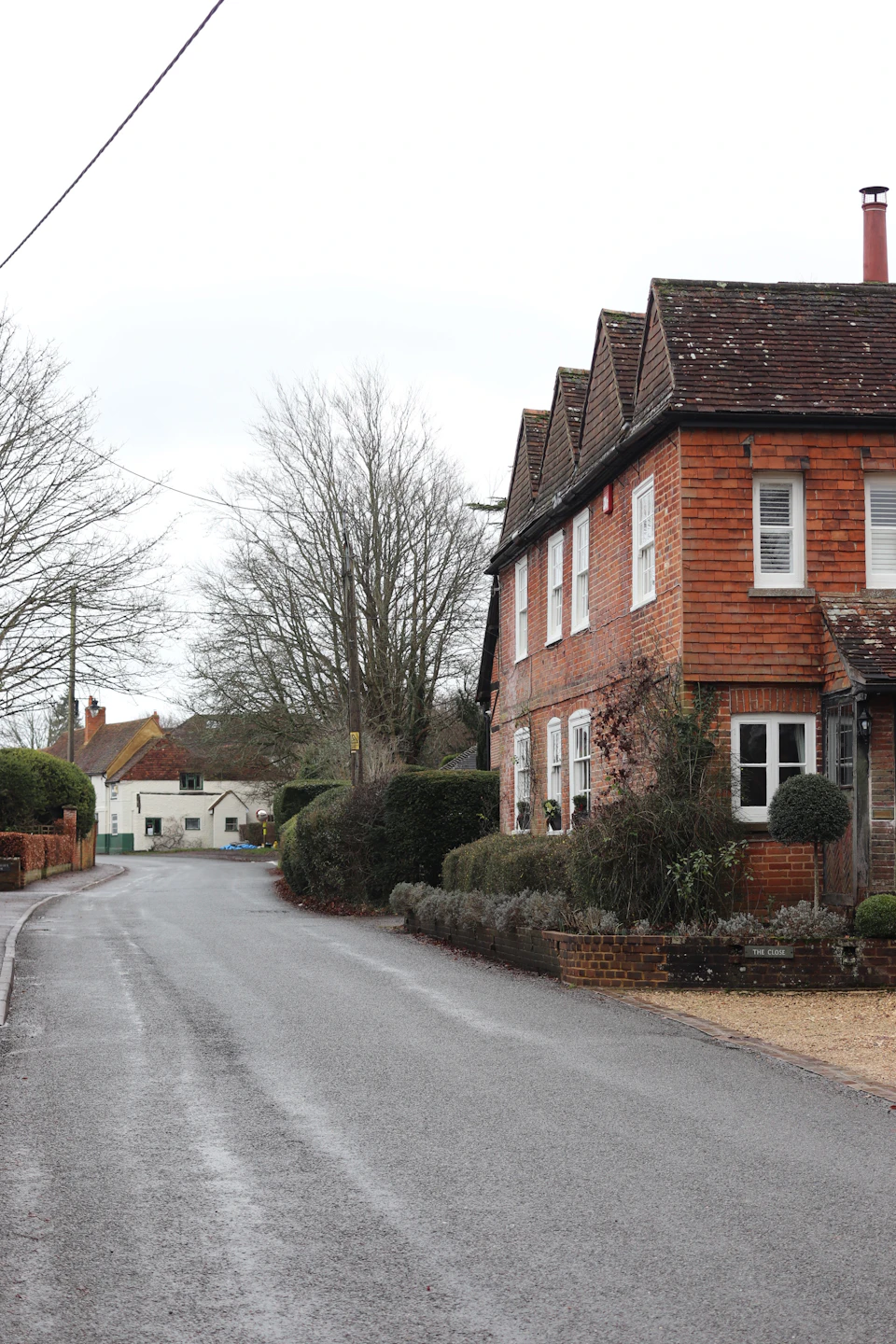 Quaint two-story brick house with red roof and white windows on a tree-lined street corner