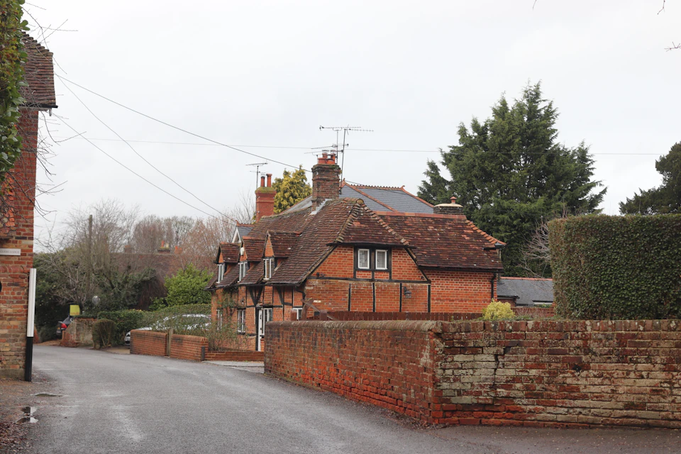 Old-fashioned brick house with red roof on street corner surrounded by stone wall and sidewalk