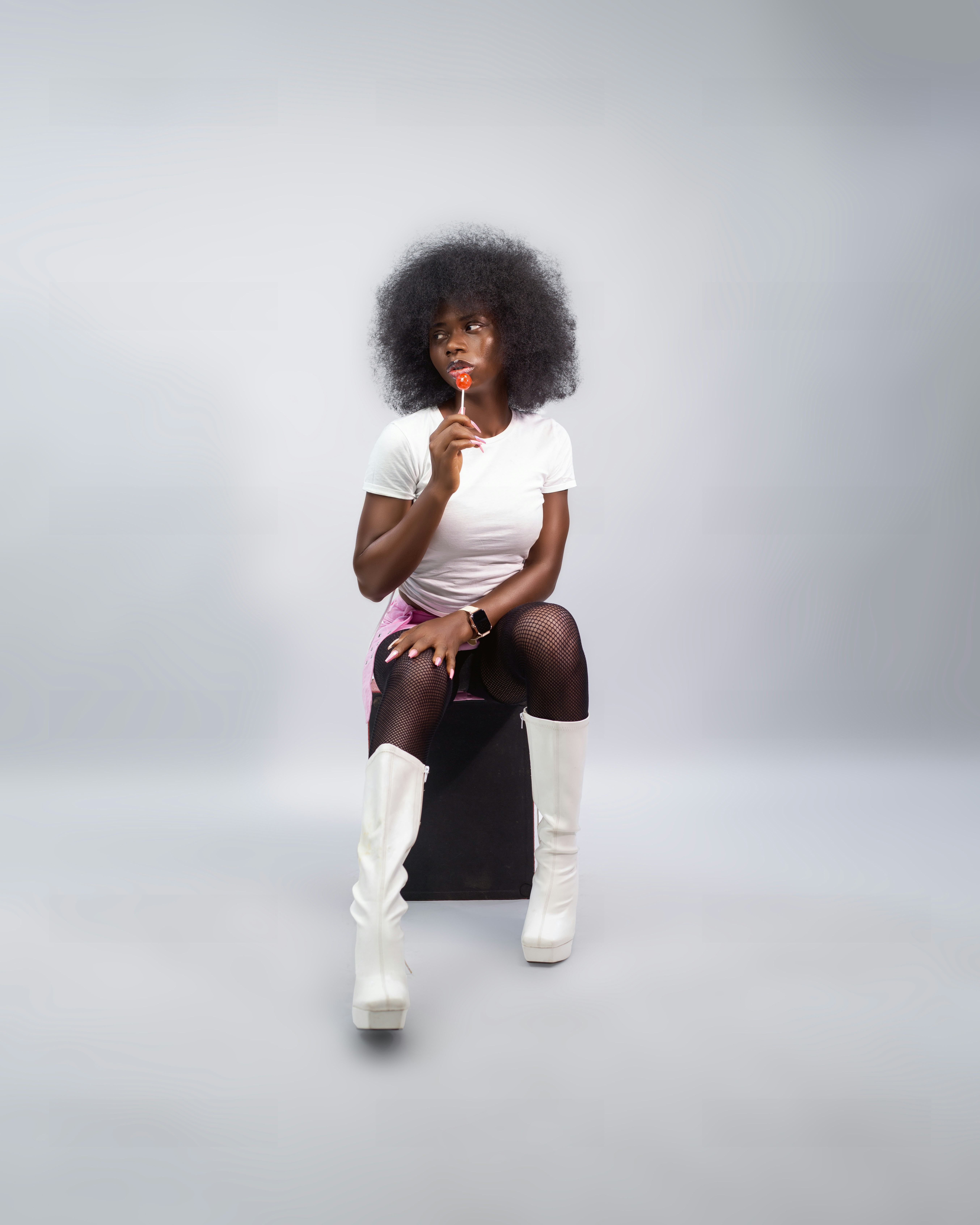 Woman with afro hair wearing white boots, holding lollipop.