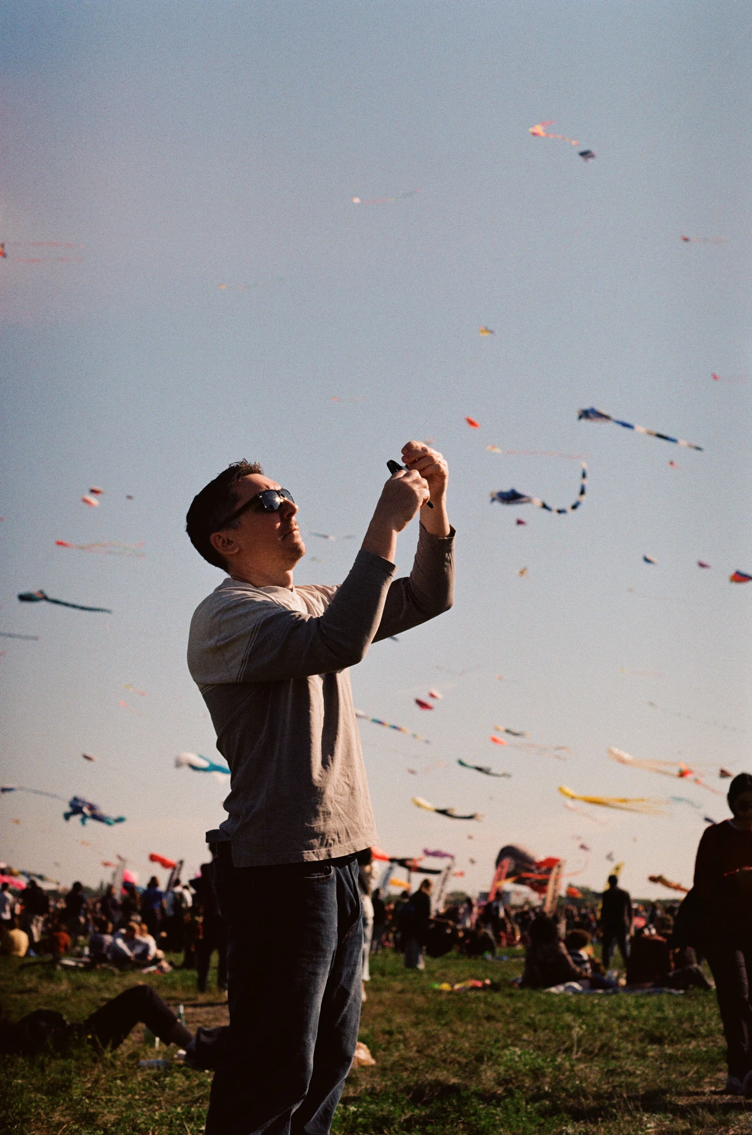 A man in sunglasses holding his kite line at a busy kite festival