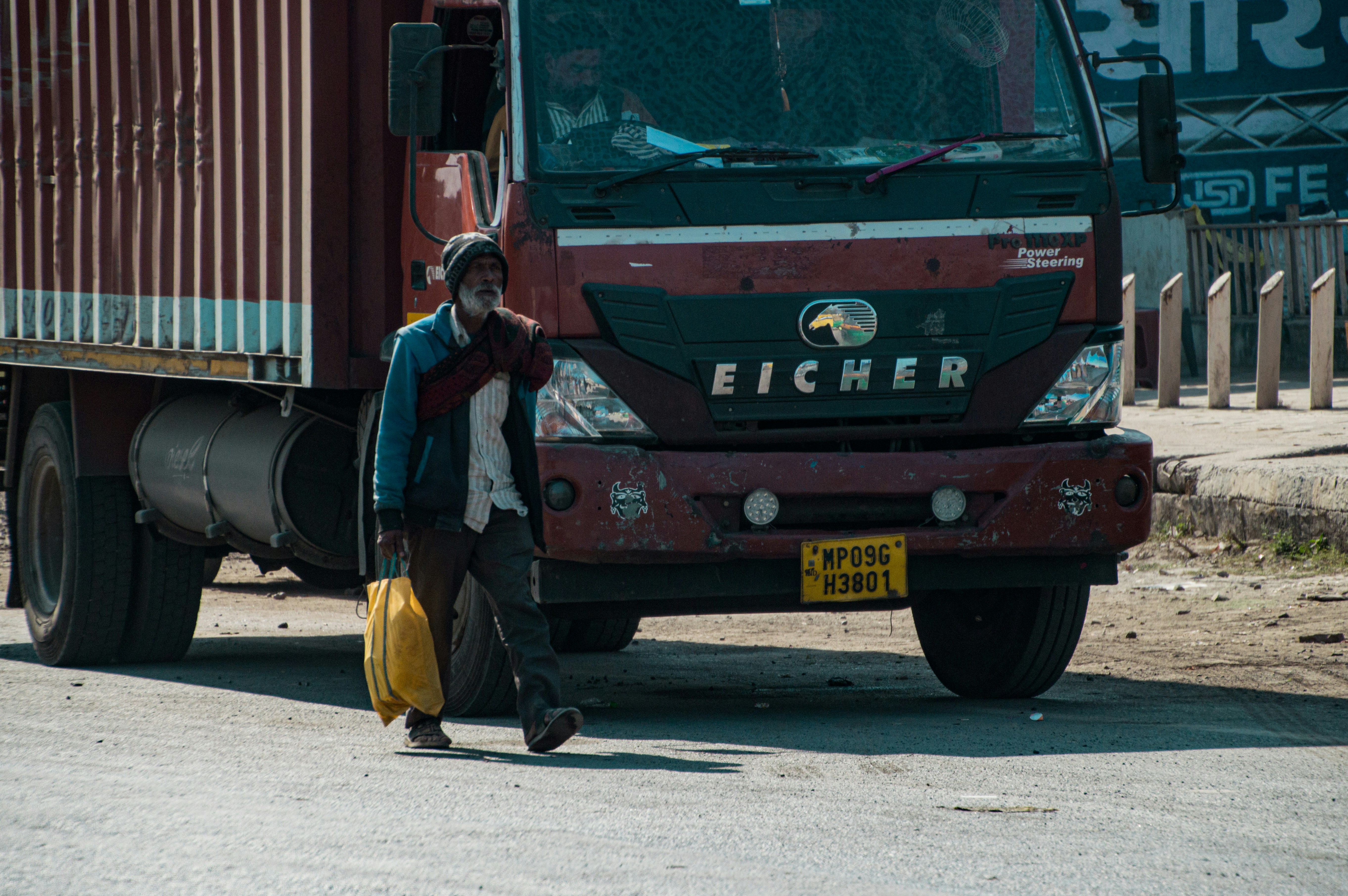 Man walks past a large truck carrying a yellow container.