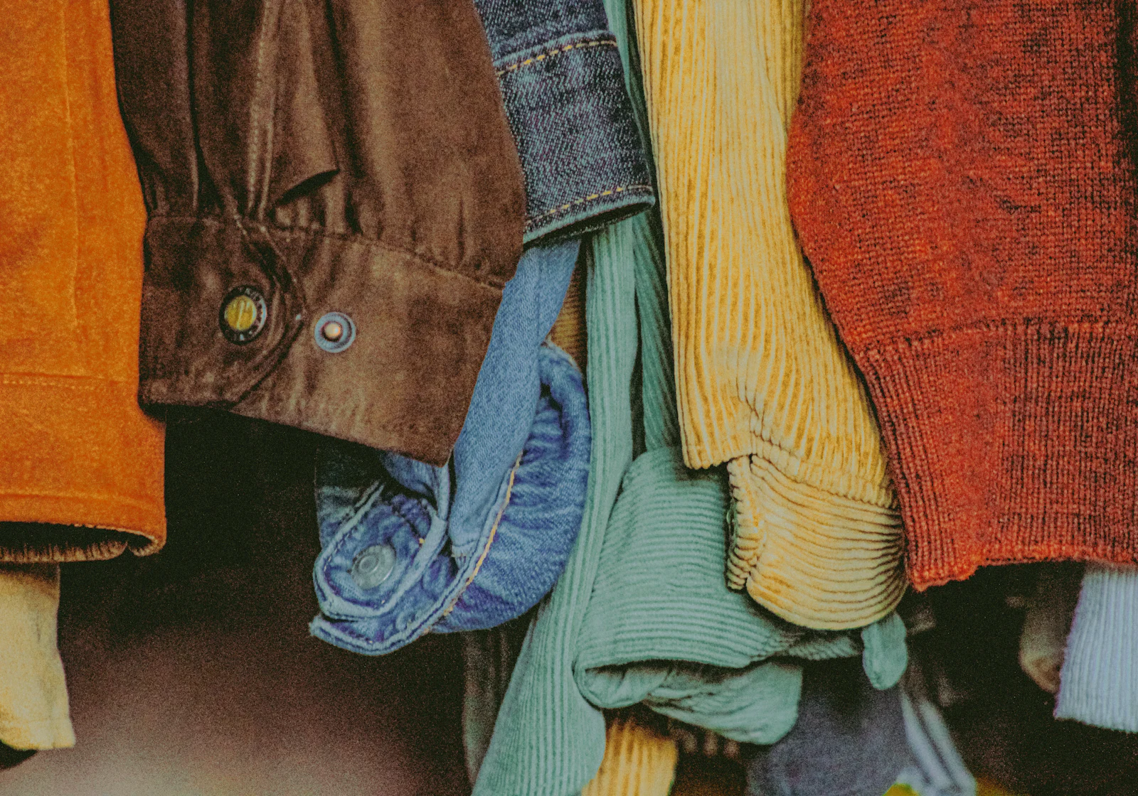 A rail of corduroy and knitwear in rust, mustard and green, seen close.