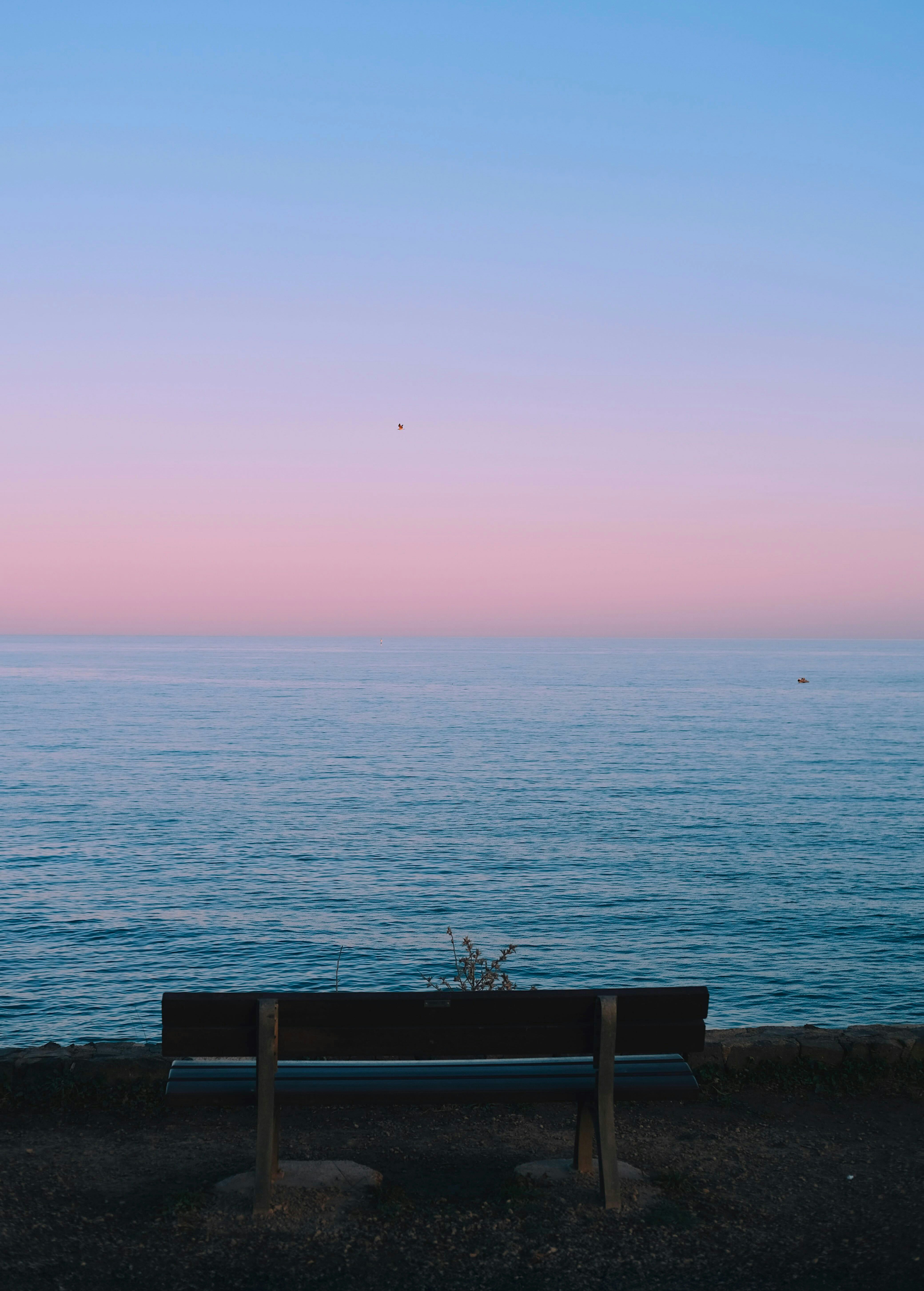 A wooden bench overlooks the ocean at sunset.