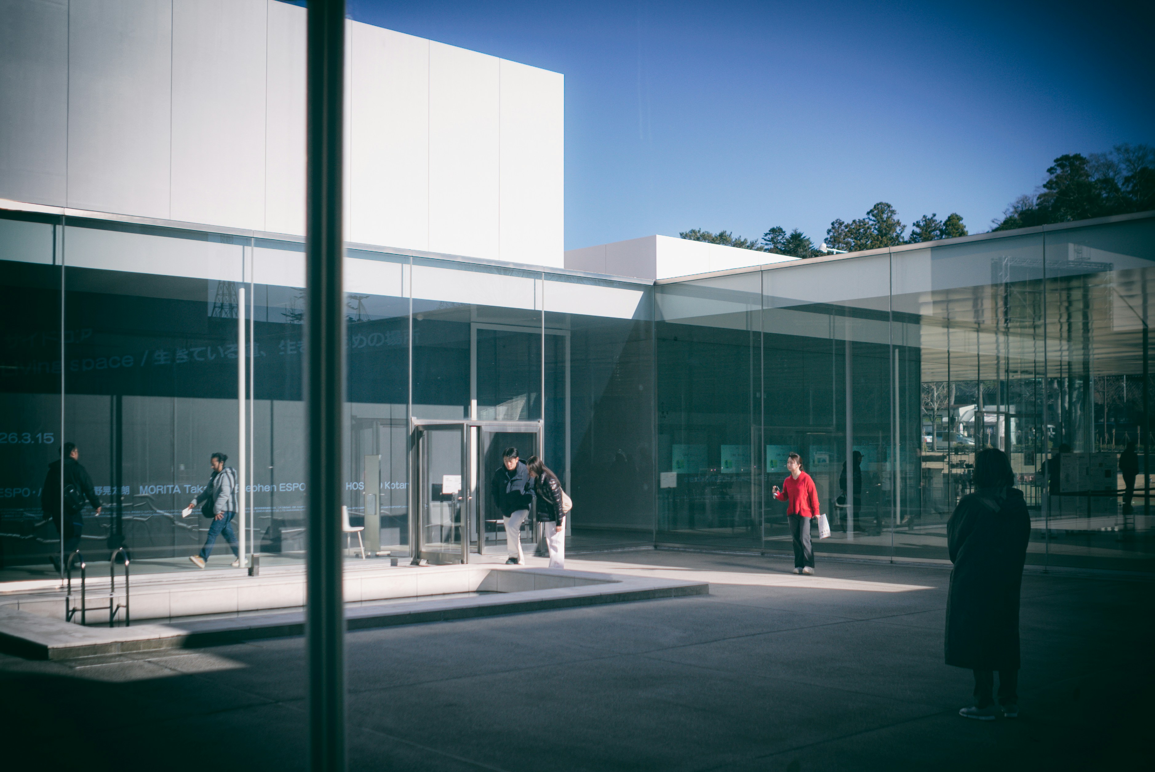 People walking near a modern building with glass walls.