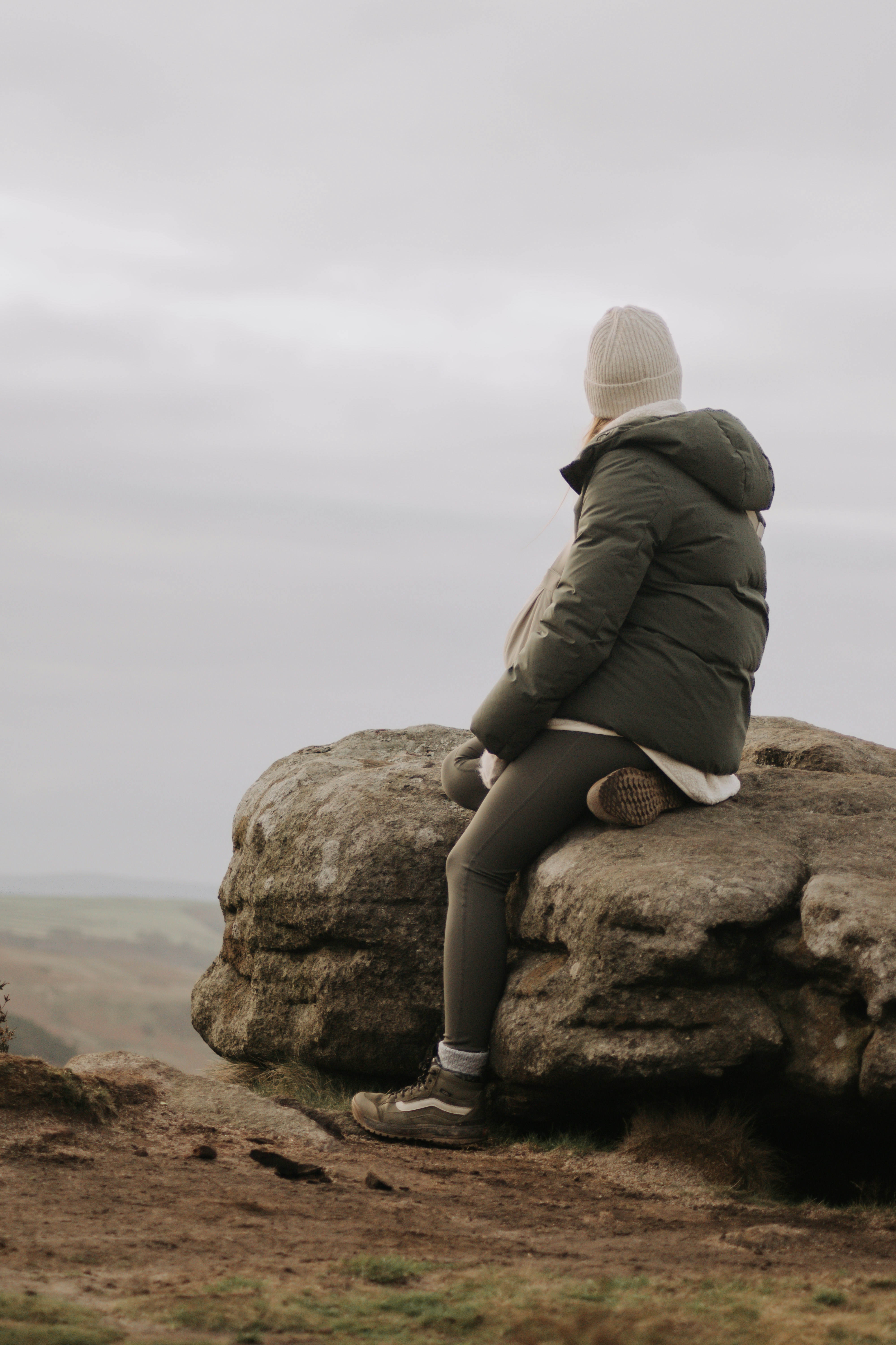 Woman in winter clothing sits on a rock overlooking landscape