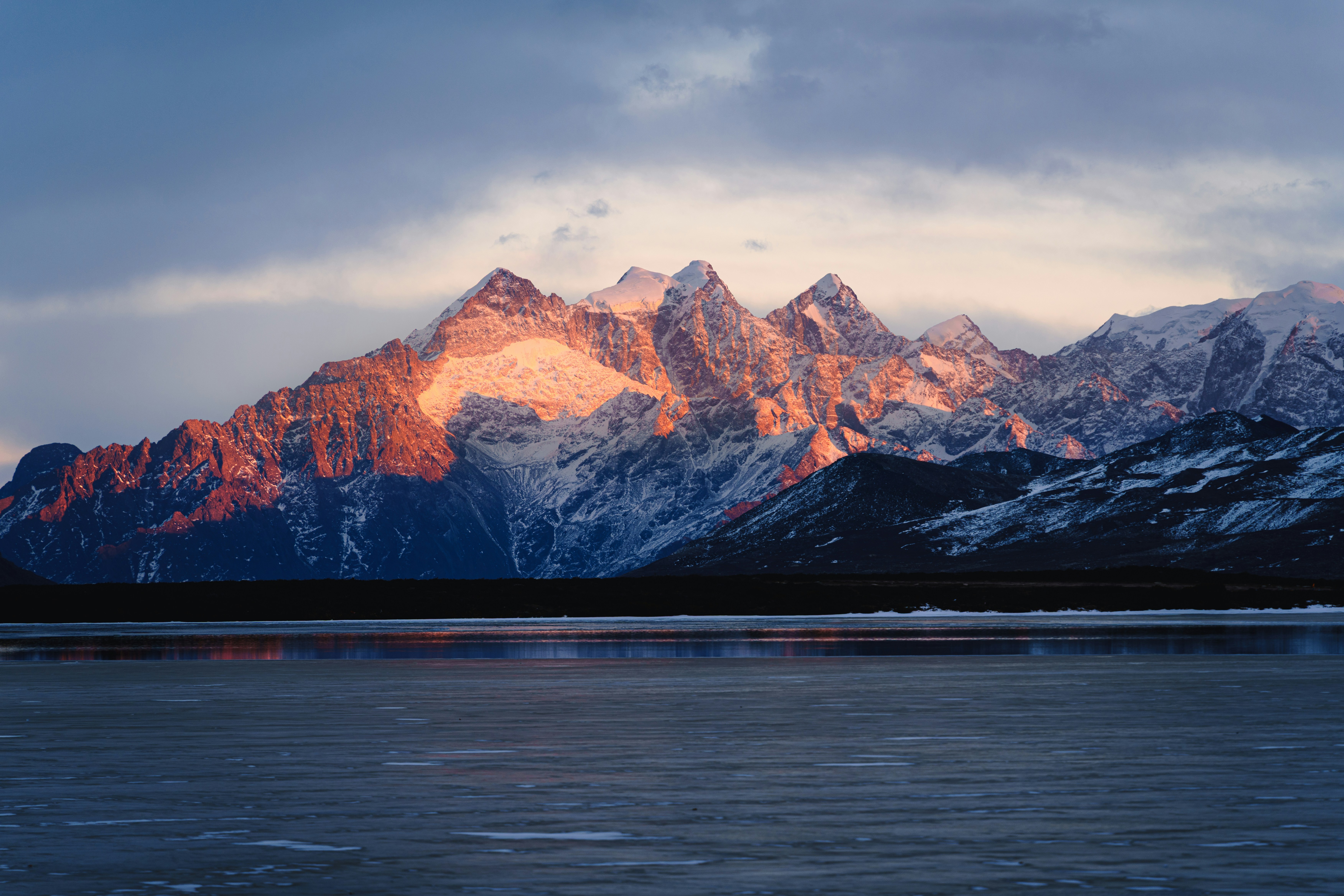 Snow-capped mountains illuminated by sunset over frozen lake.