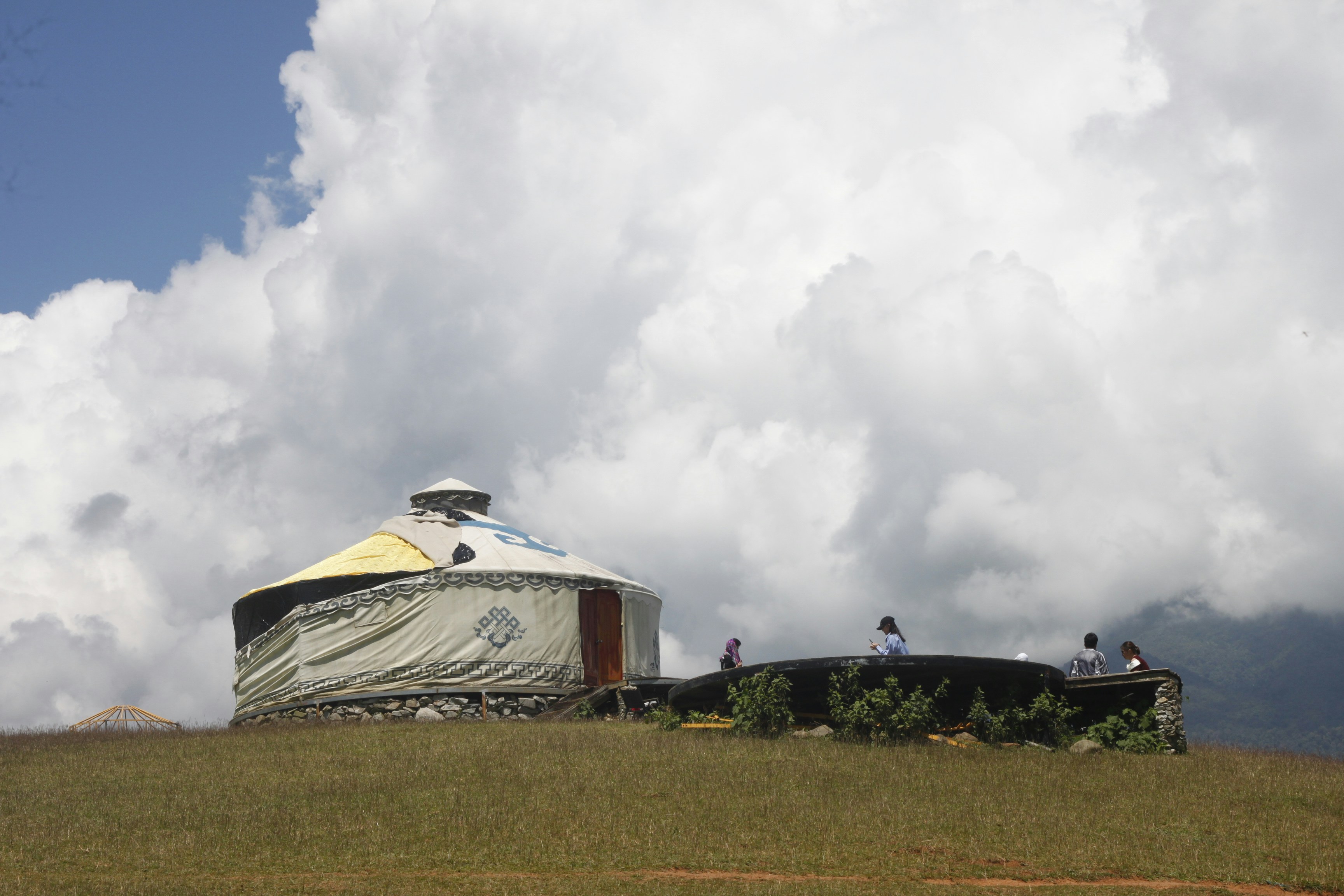 Yurt on a grassy hill with large clouds