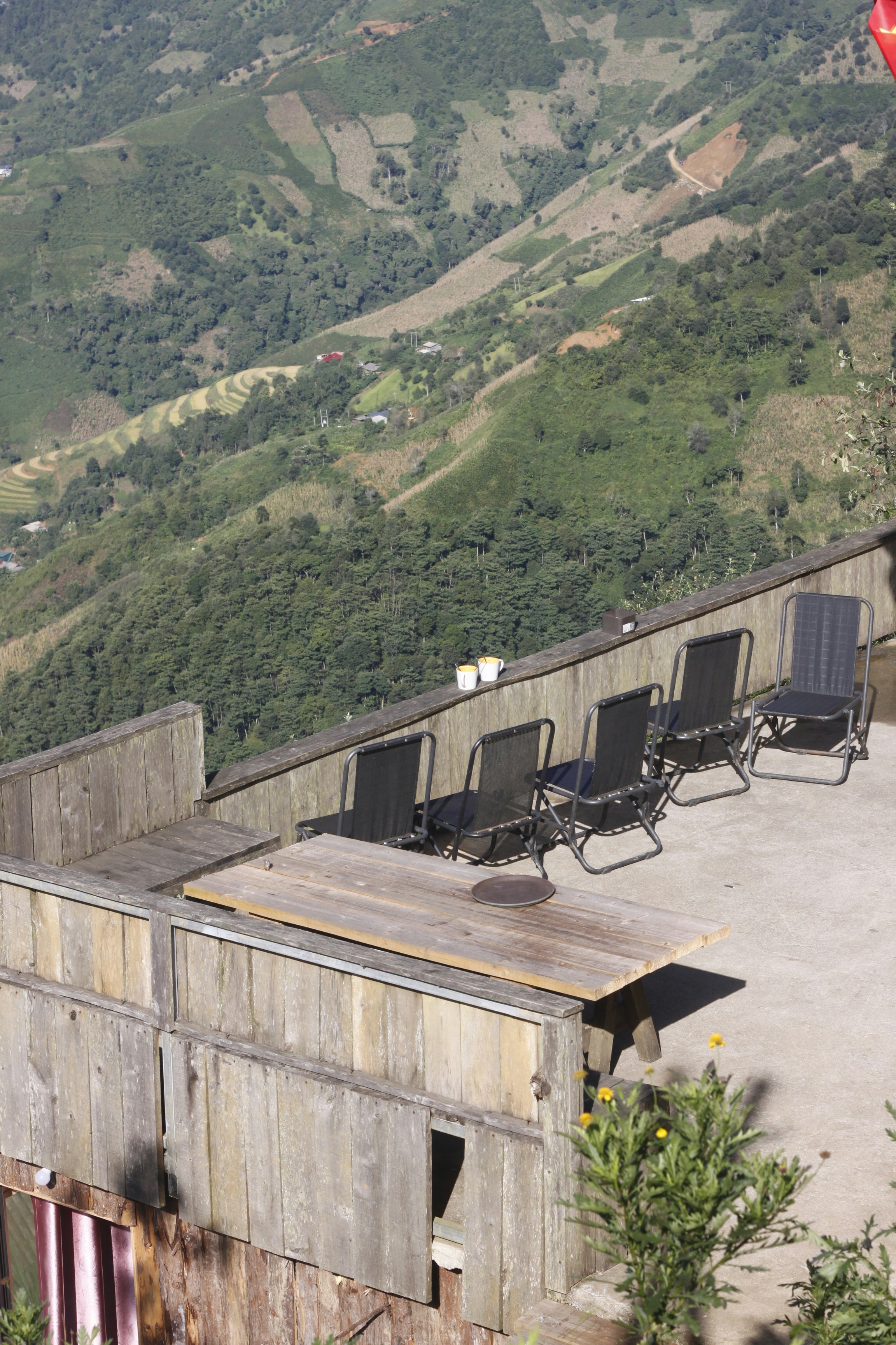 Deck chairs and table on a wooden balcony overlooking hills.