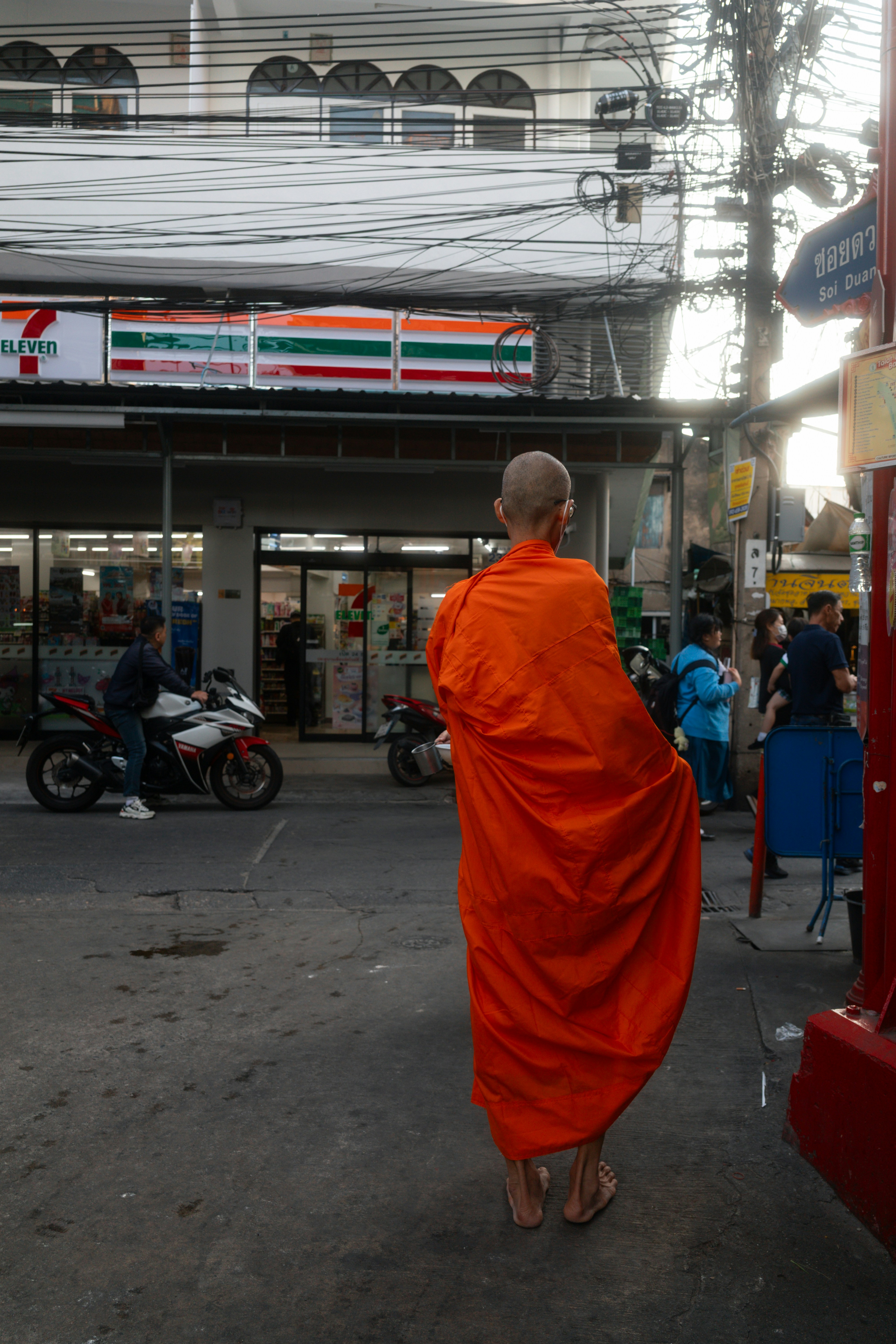 Monk in orange robes walks down a street.