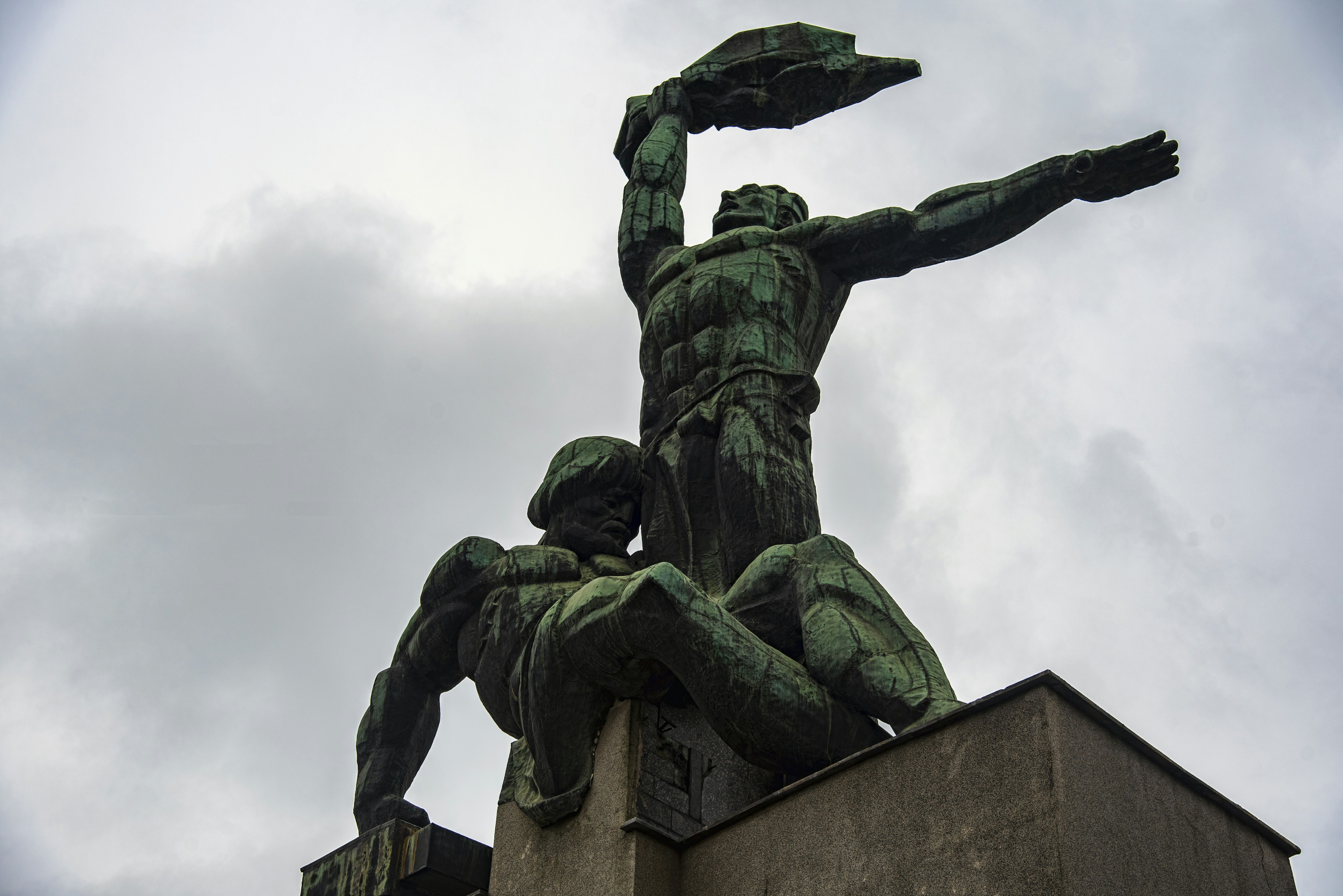 Two bronze figures on a monument against a cloudy sky