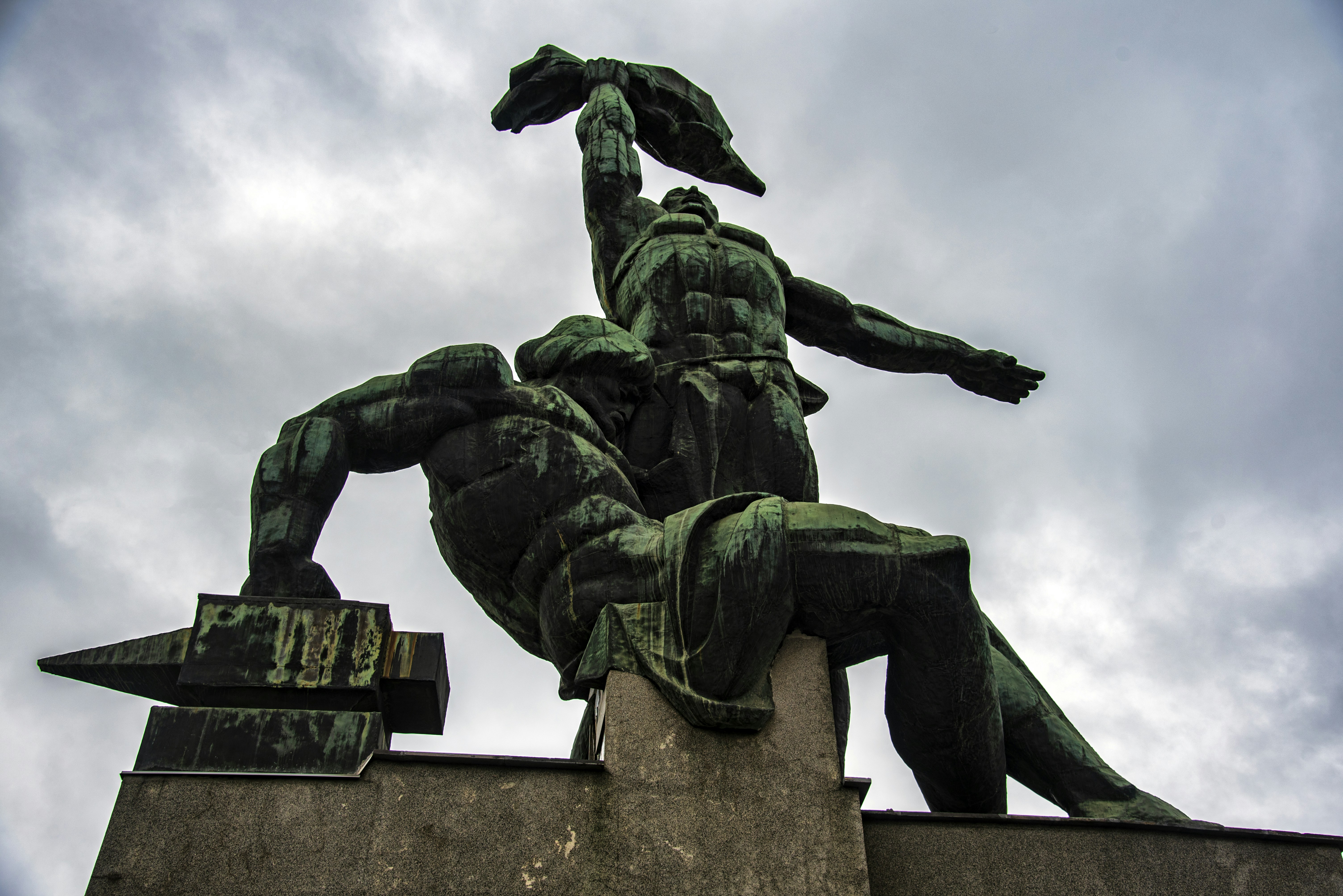 Bronze statue of two muscular men against cloudy sky