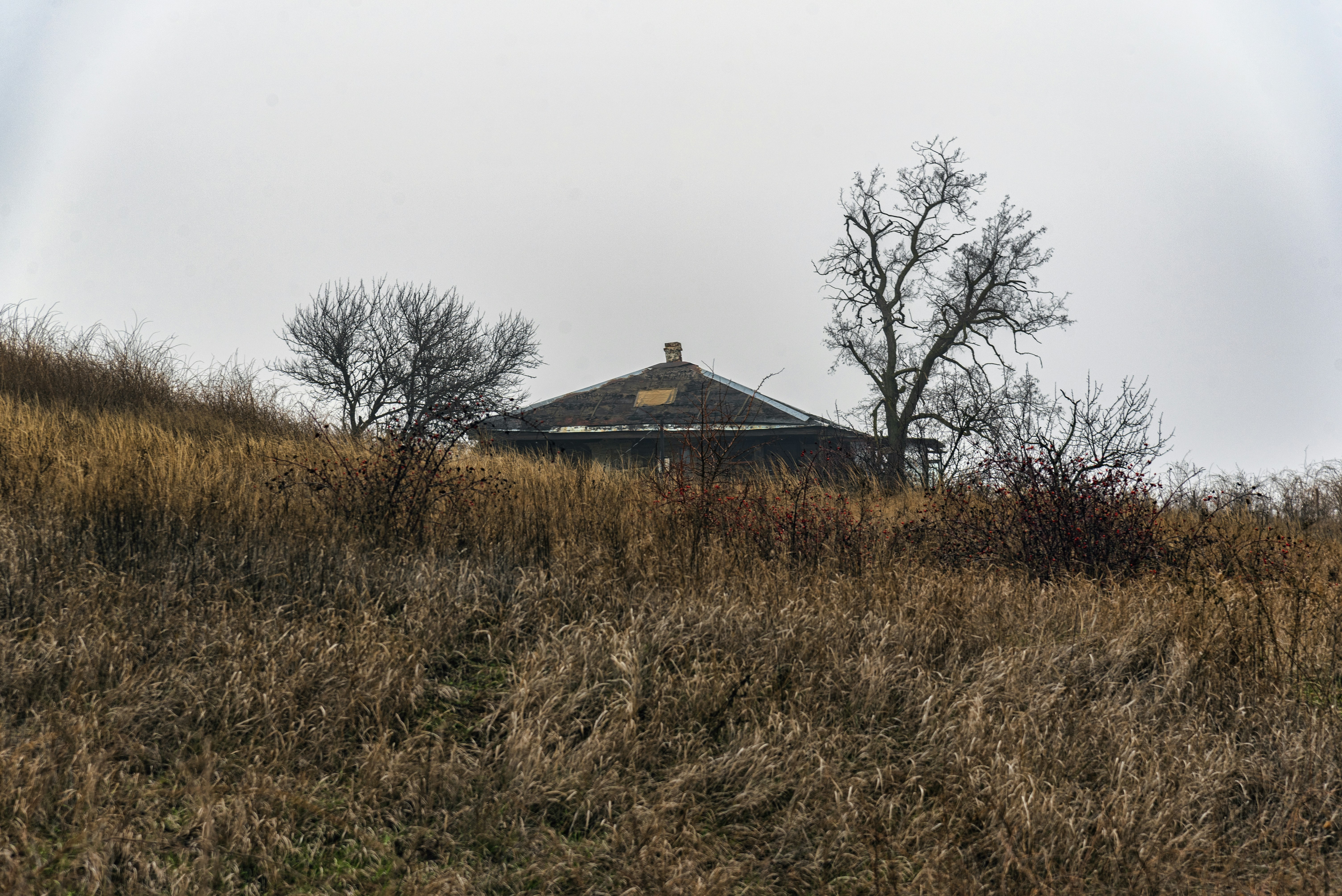 An old house sits on a hill with dry grass.