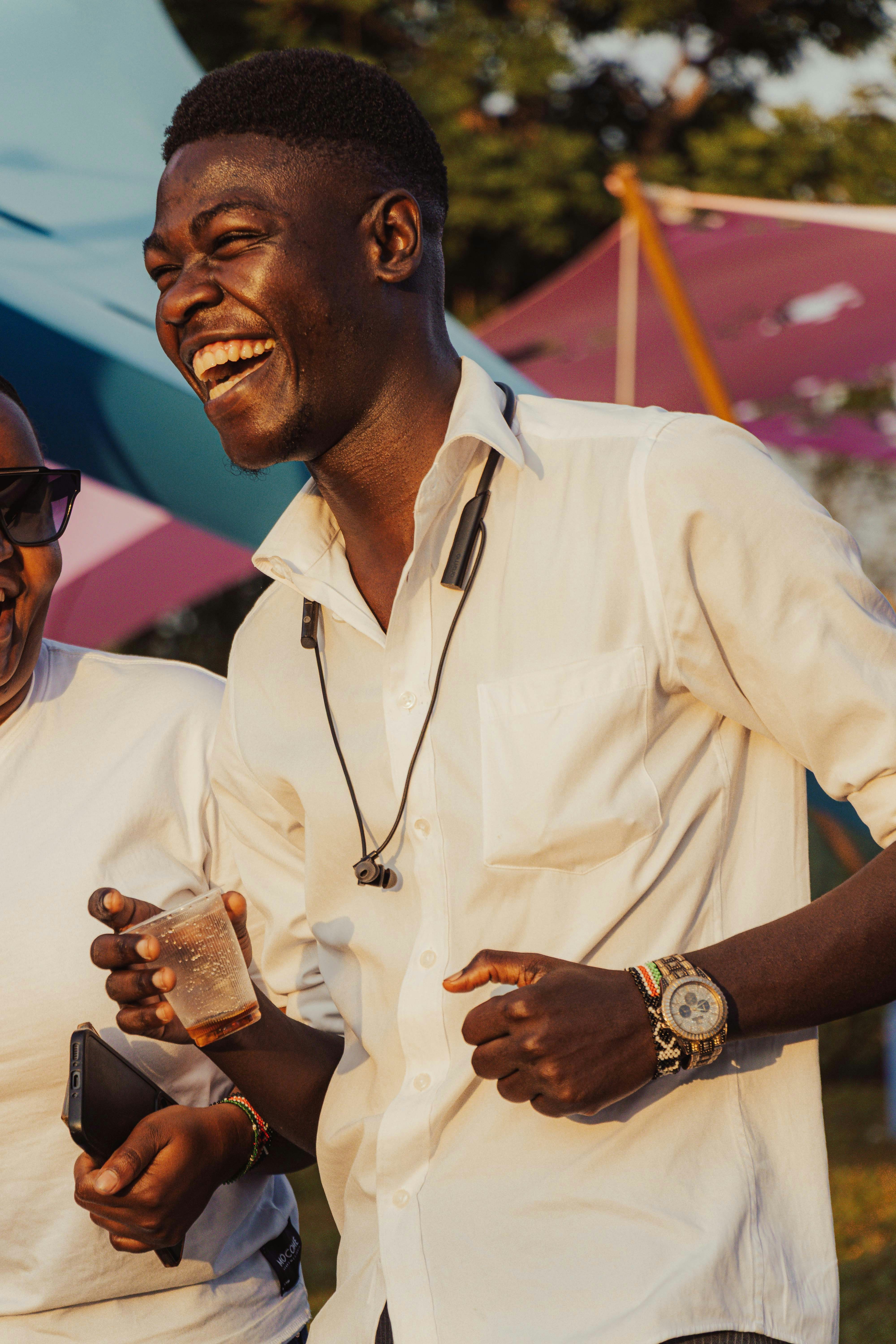 A man in a white shirt laughs holding a drink