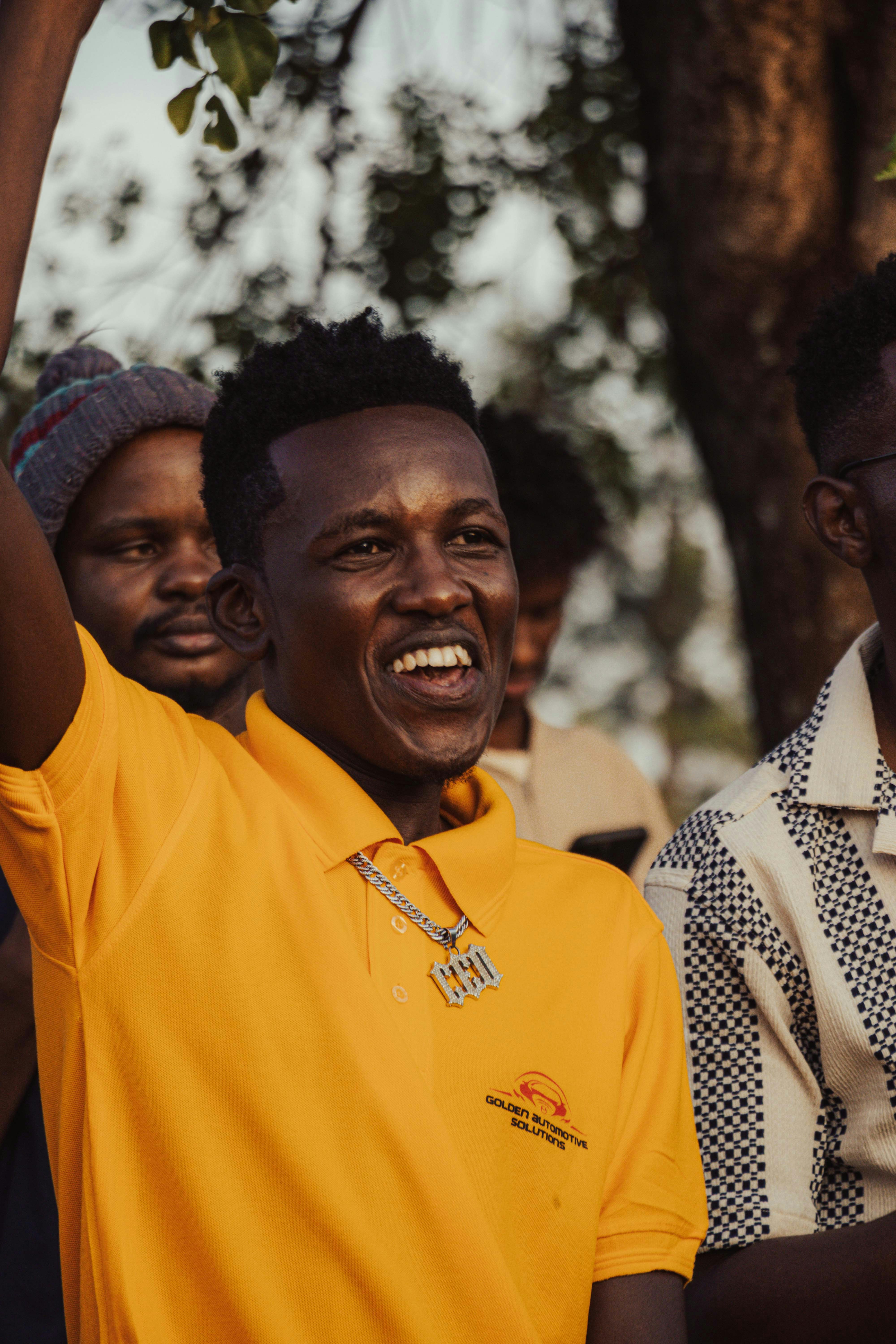 Man in yellow shirt with arms raised, smiling.