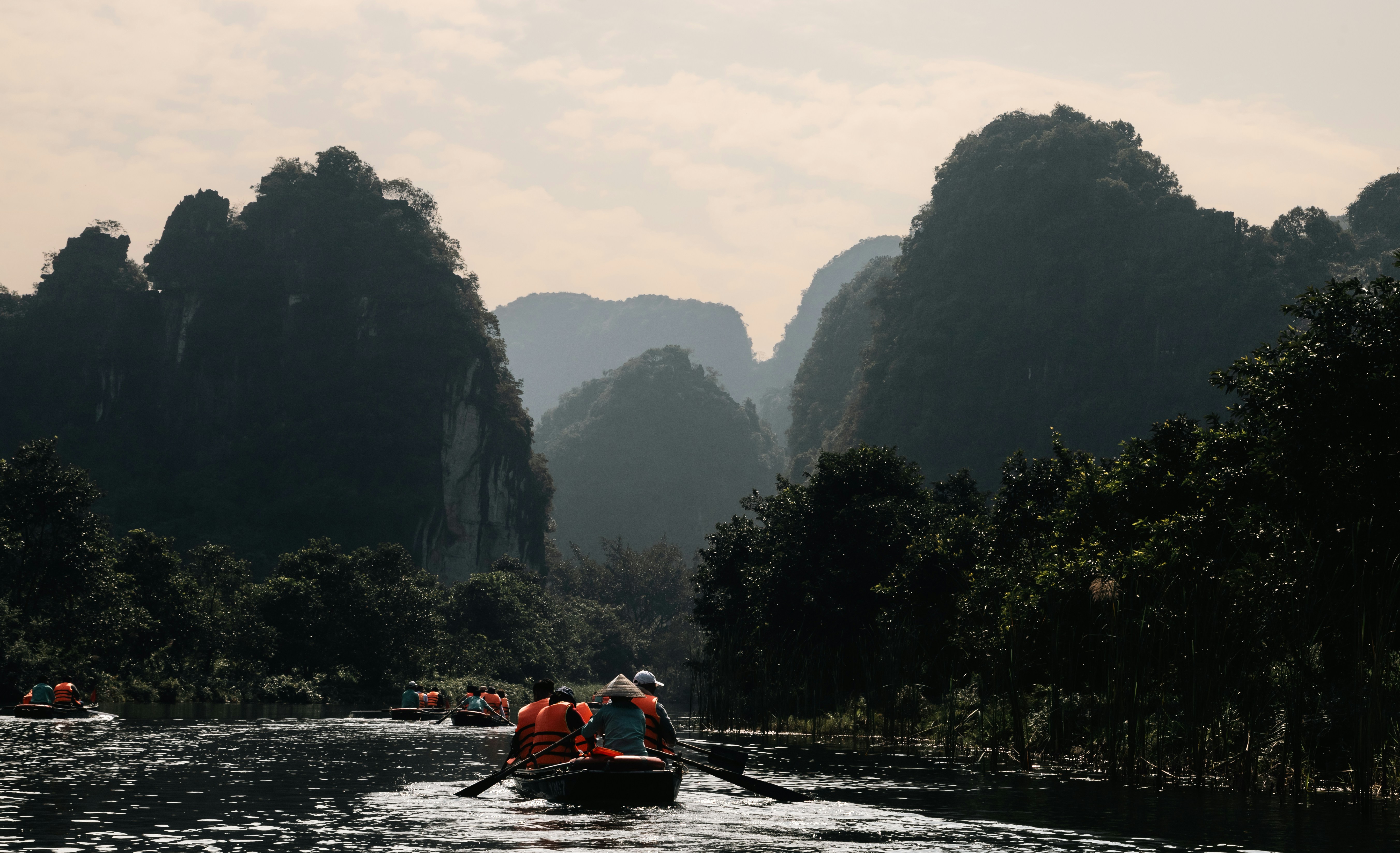 Le barche navigano su un fiume circondato da rigogliose montagne carsiche verdi.